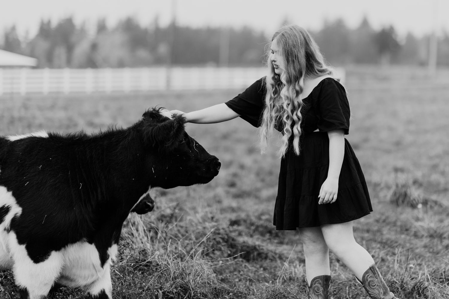 A black and white photo of a person in a dress petting a calf in a rural field.