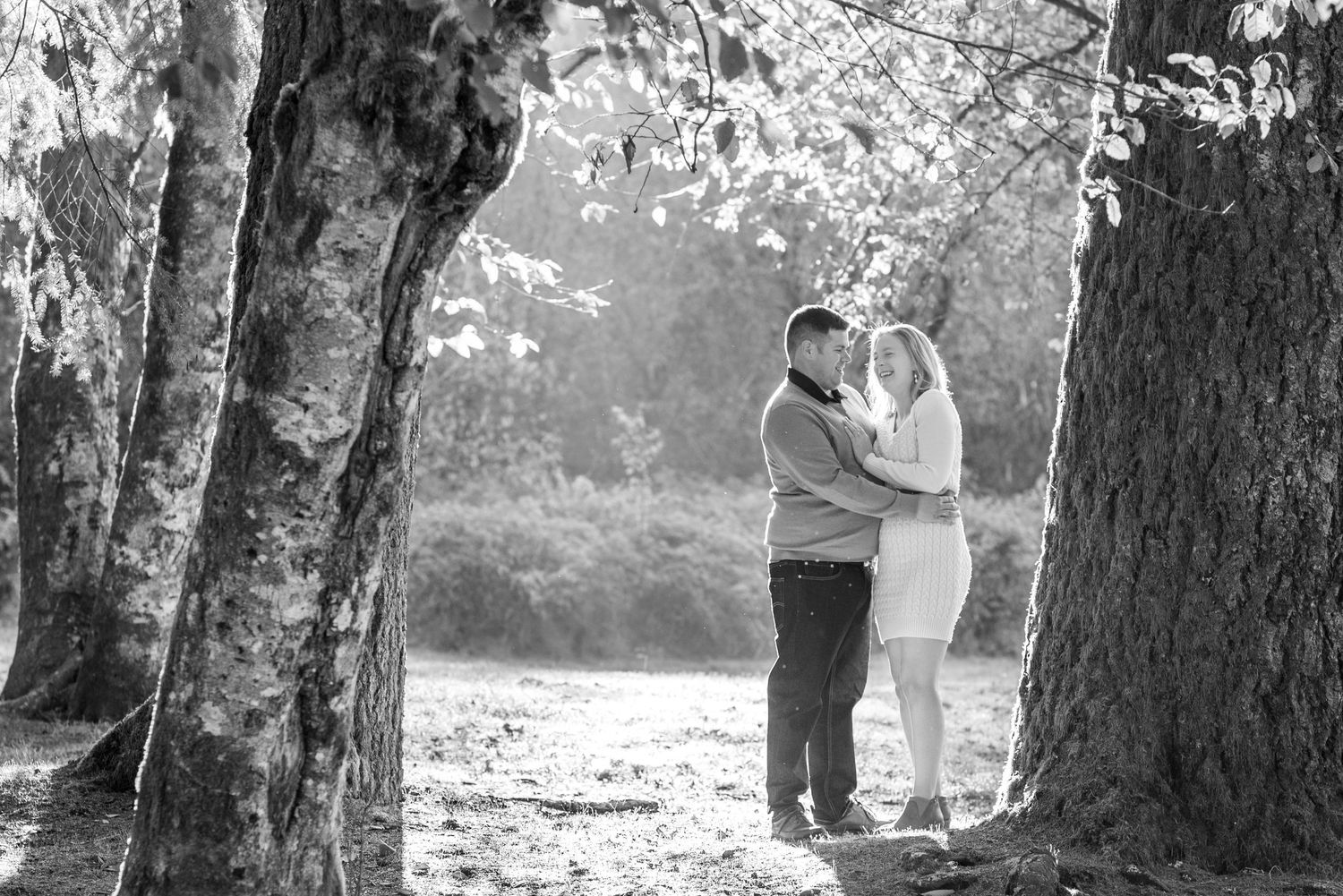 Black and white photo of family posing together among tall trees in forest setting.