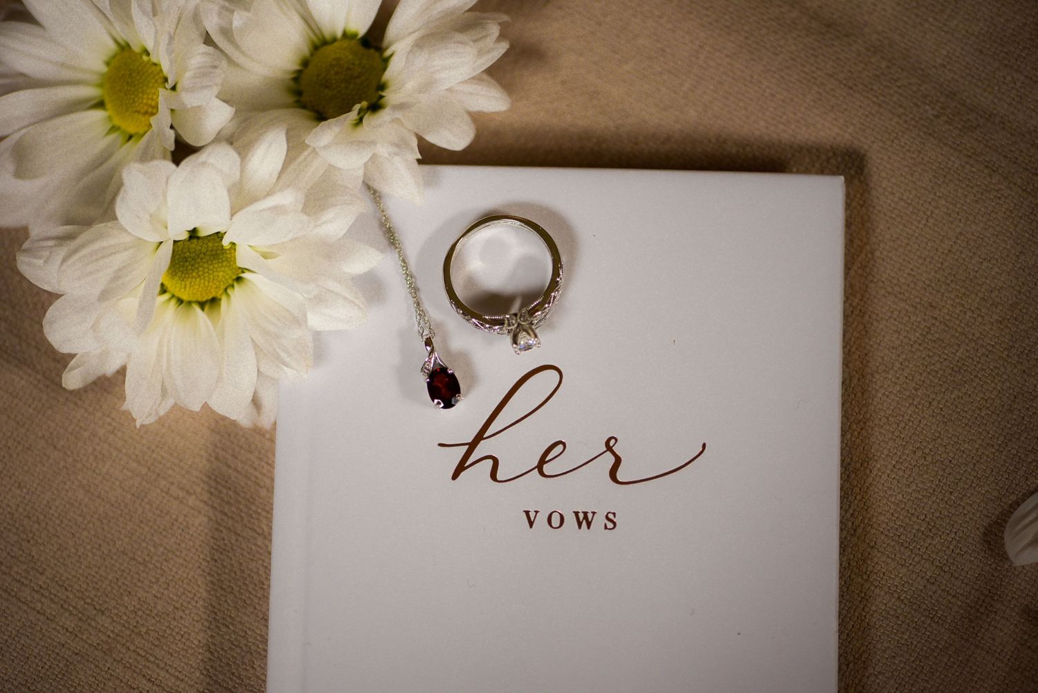Wedding rings and daisies arranged with vows card on neutral background.