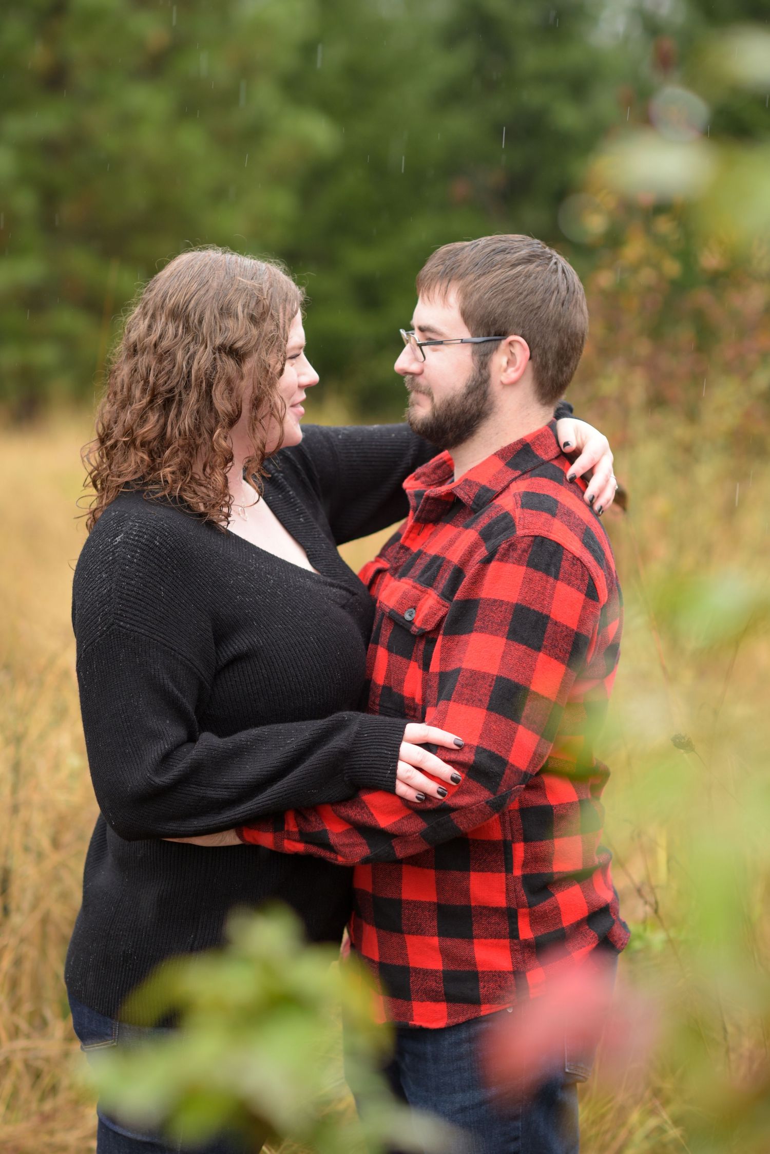A couple embraces and laughs together in a natural outdoor setting with fall foliage.