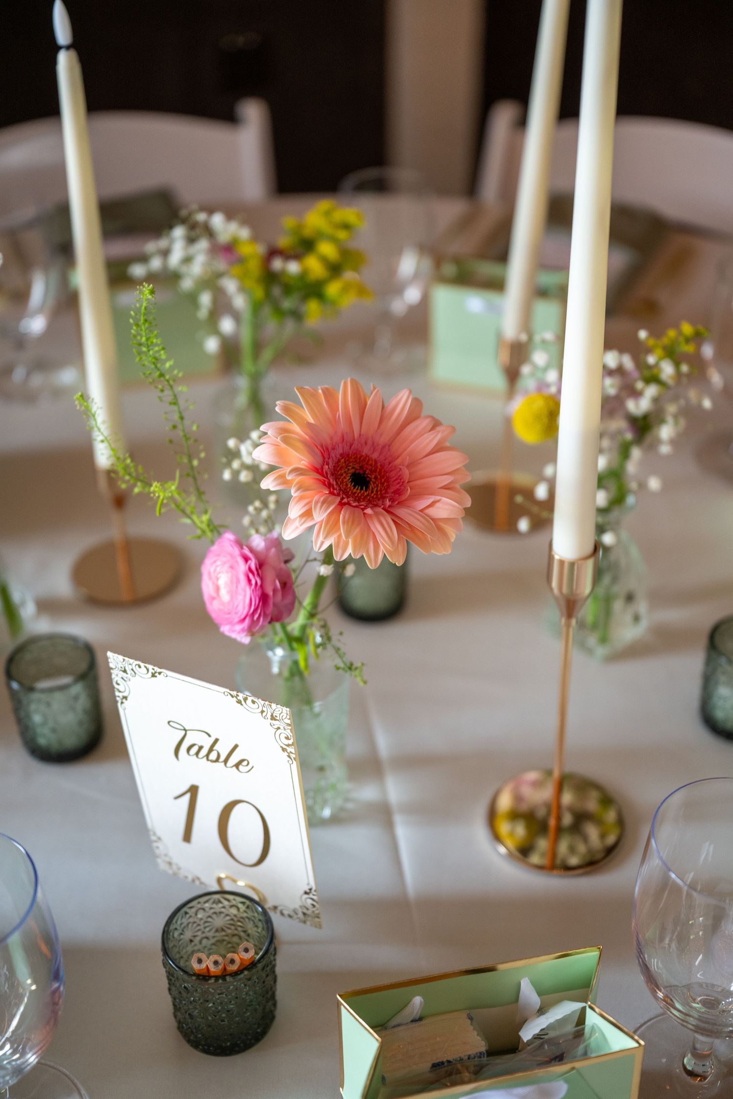 Elegant wedding table 10 centerpiece with pink gerbera daisy, ranunculus, tall white candles, and small bud vases.