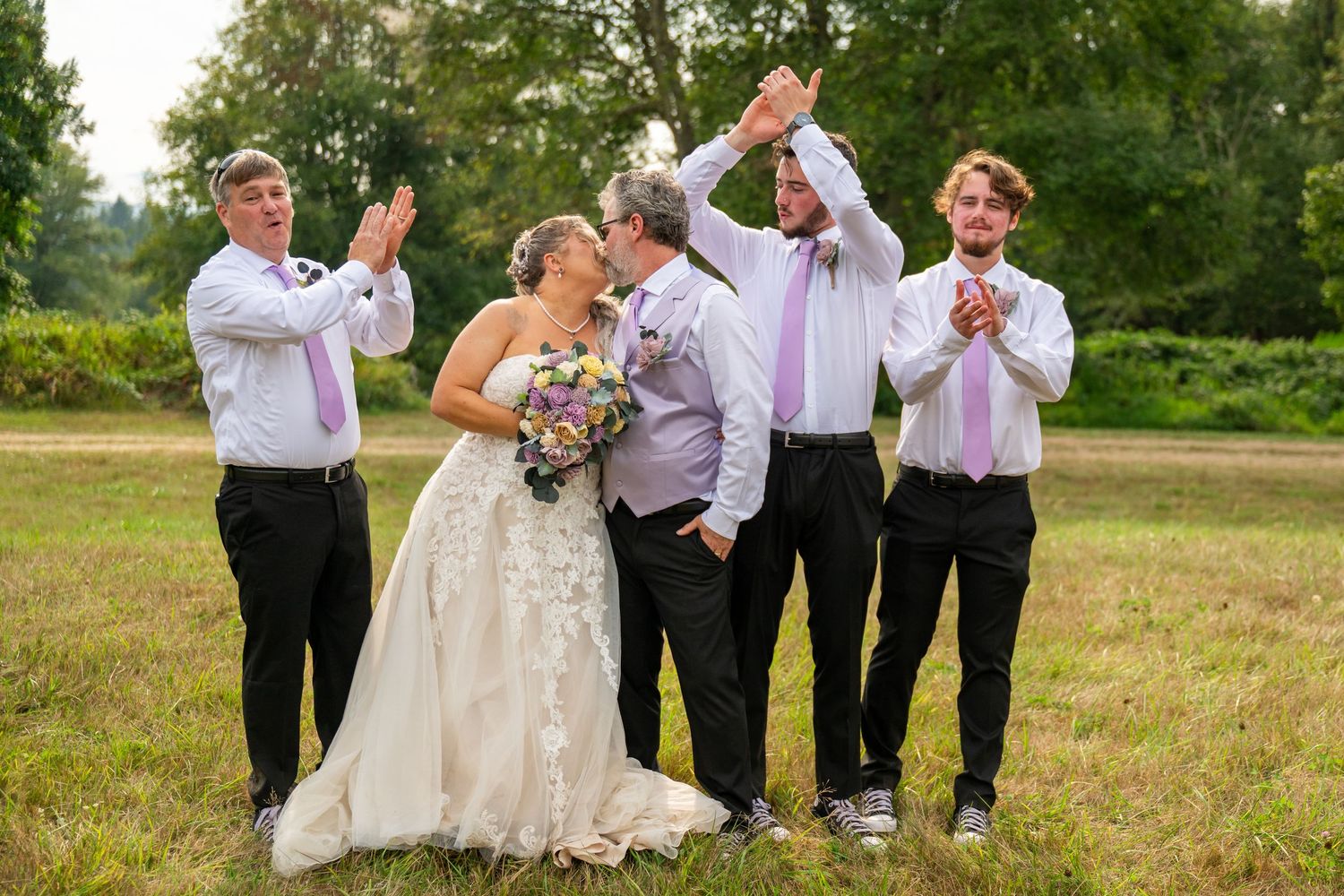 Wedding party members celebrate joyfully in an open field during sunset.