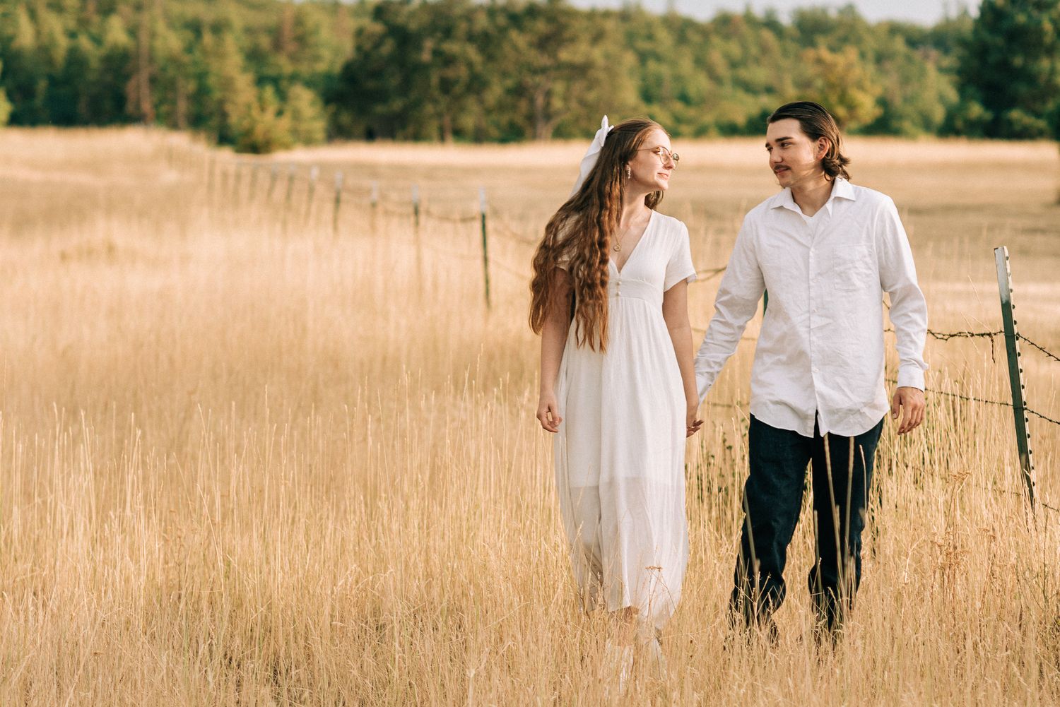 Couple walks hand in hand through a golden wheat field at sunset.