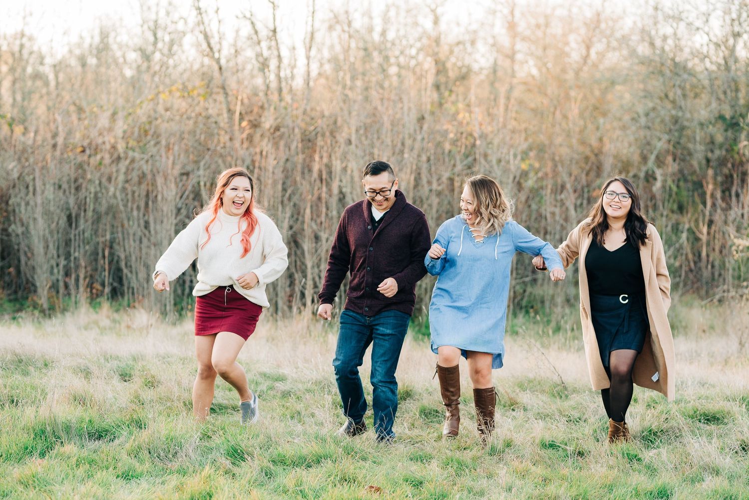 Happy family of four walking and laughing together through an open field with tall dried grasses.