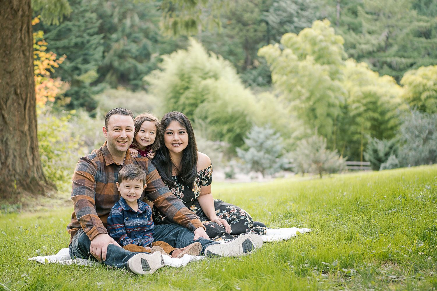 Family relaxing together on blanket during outdoor photo session in wooded park.