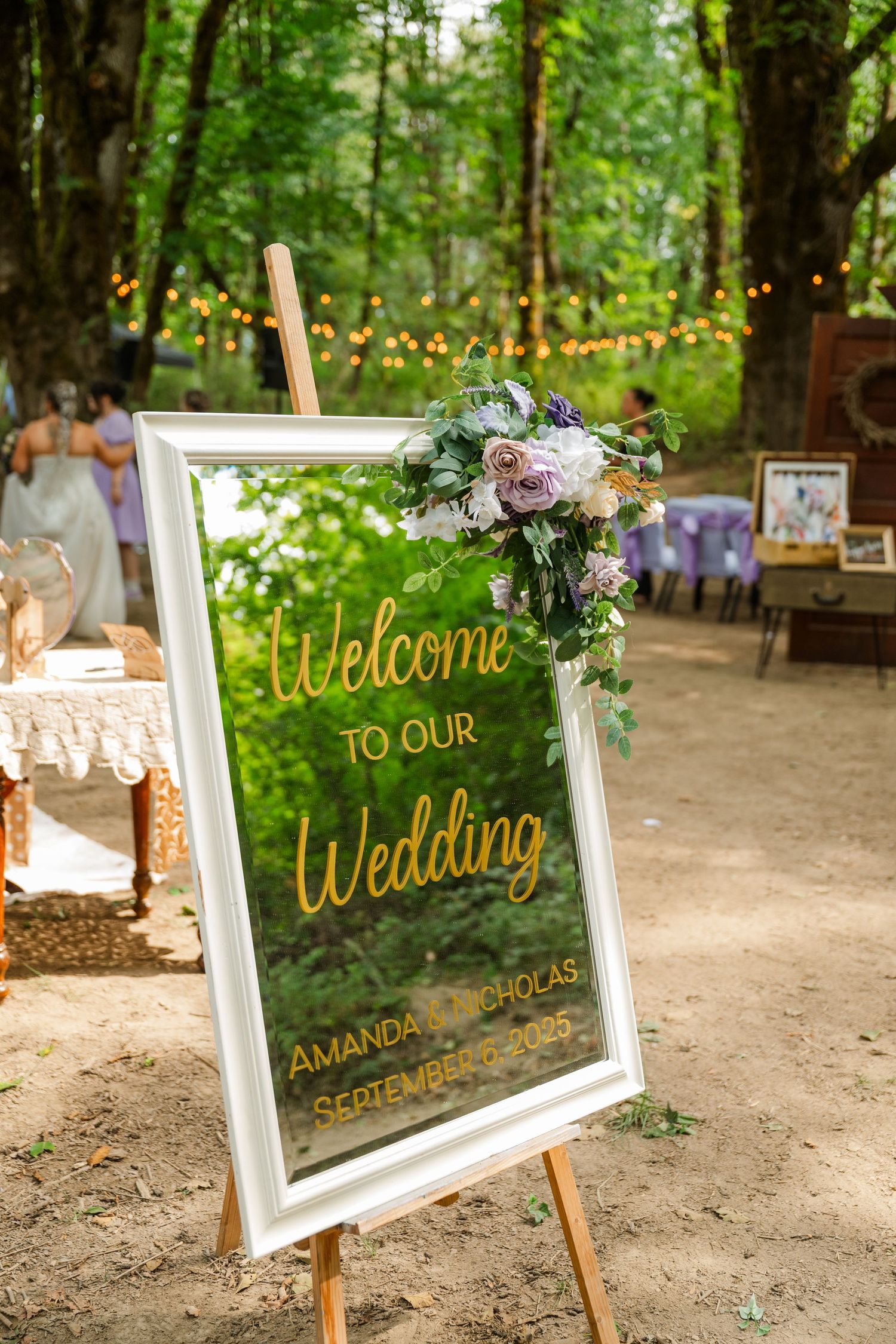 Elegant mirrored wedding welcome sign reading Amanda and Nicholas September 2025 decorated with floral arrangement.