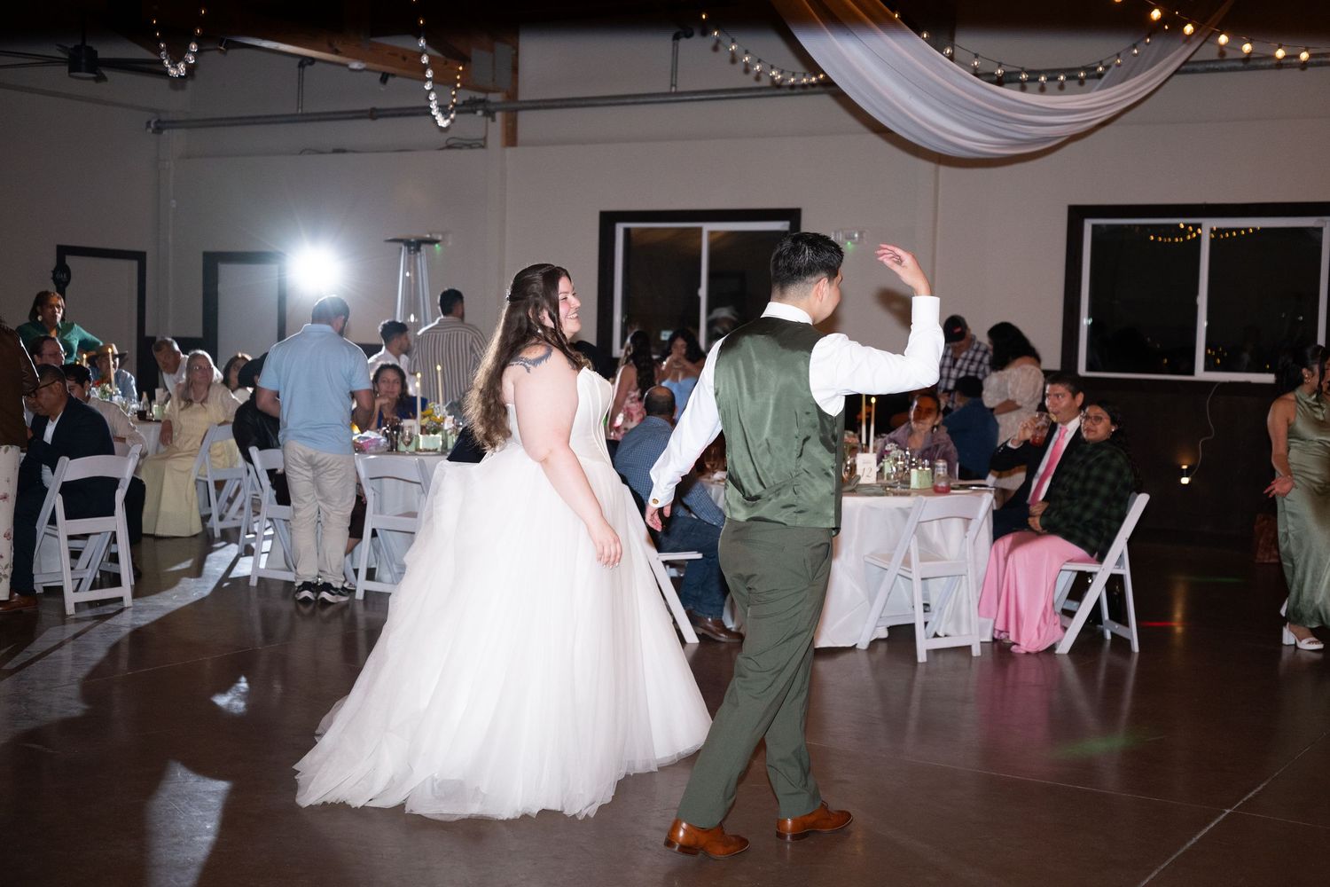 Bride and groom share first dance at wedding reception in elegant venue with guests seated at decorated tables.