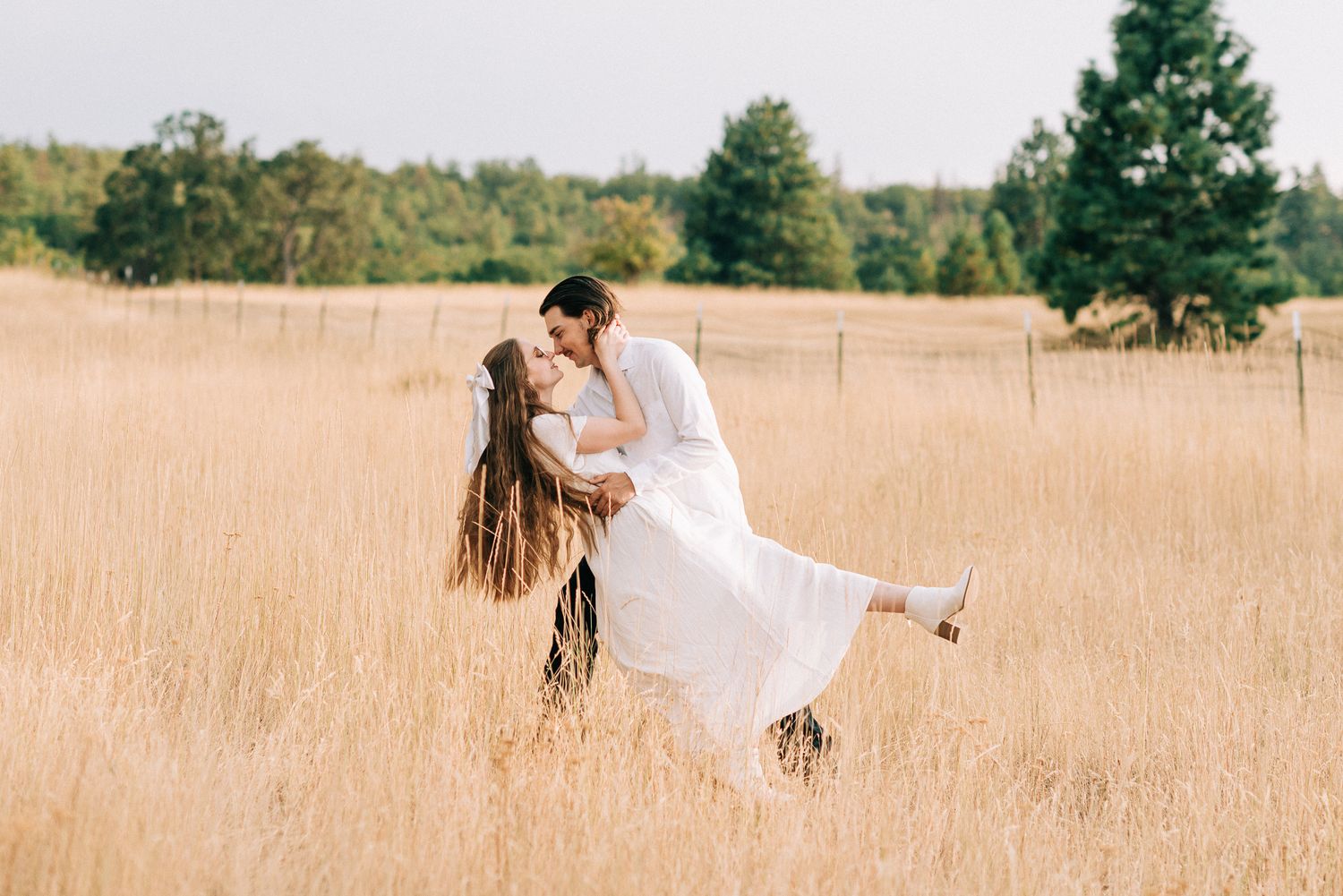 Groom dips bride in a golden wheat field during an outdoor wedding celebration on a beautiful day.