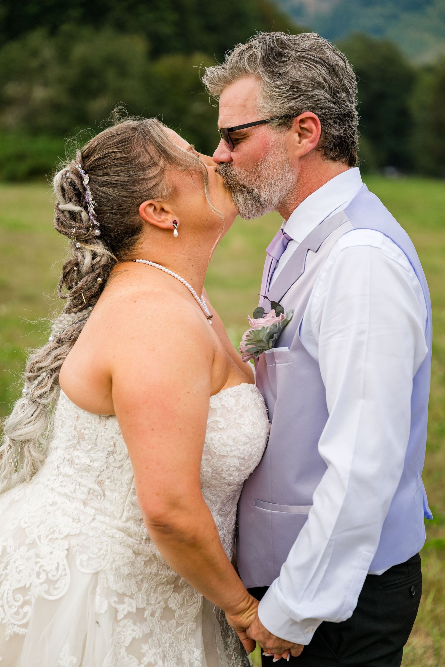 Mature bride and groom kissing tenderly in a lush green outdoor wedding setting.