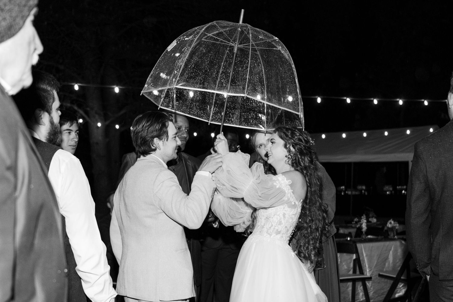 Wedding celebration under twinkling lights with dancing and umbrellas.