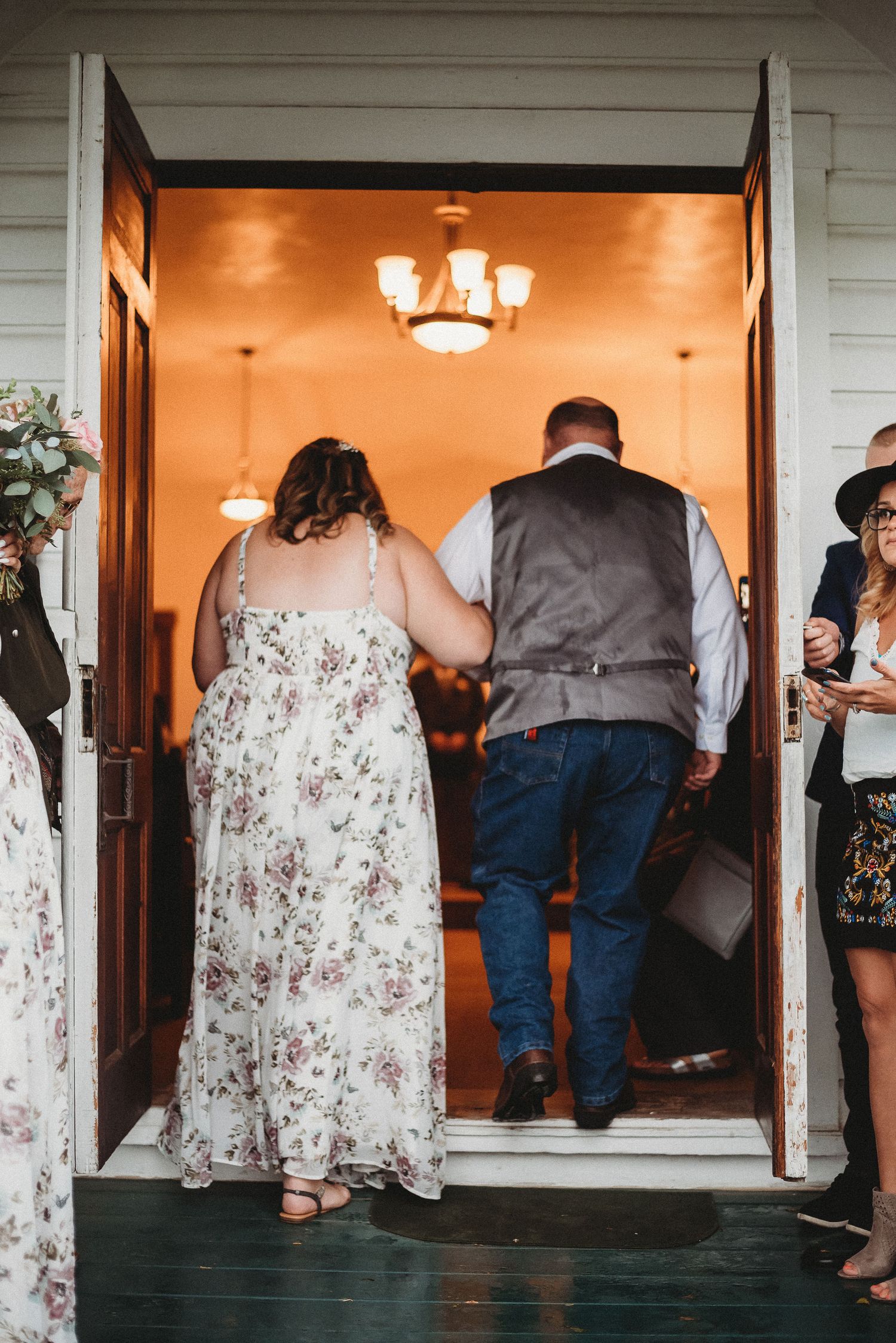 A couple enters a warmly lit doorway at a wedding venue, with the bride wearing a floral patterned dress.