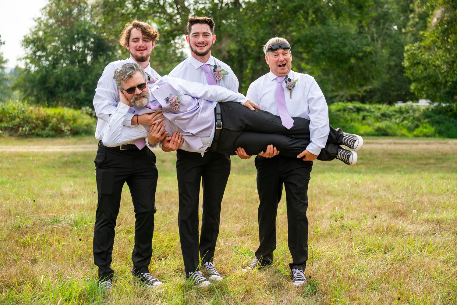 Groomsmen strike playful poses in formal attire on grassy field.