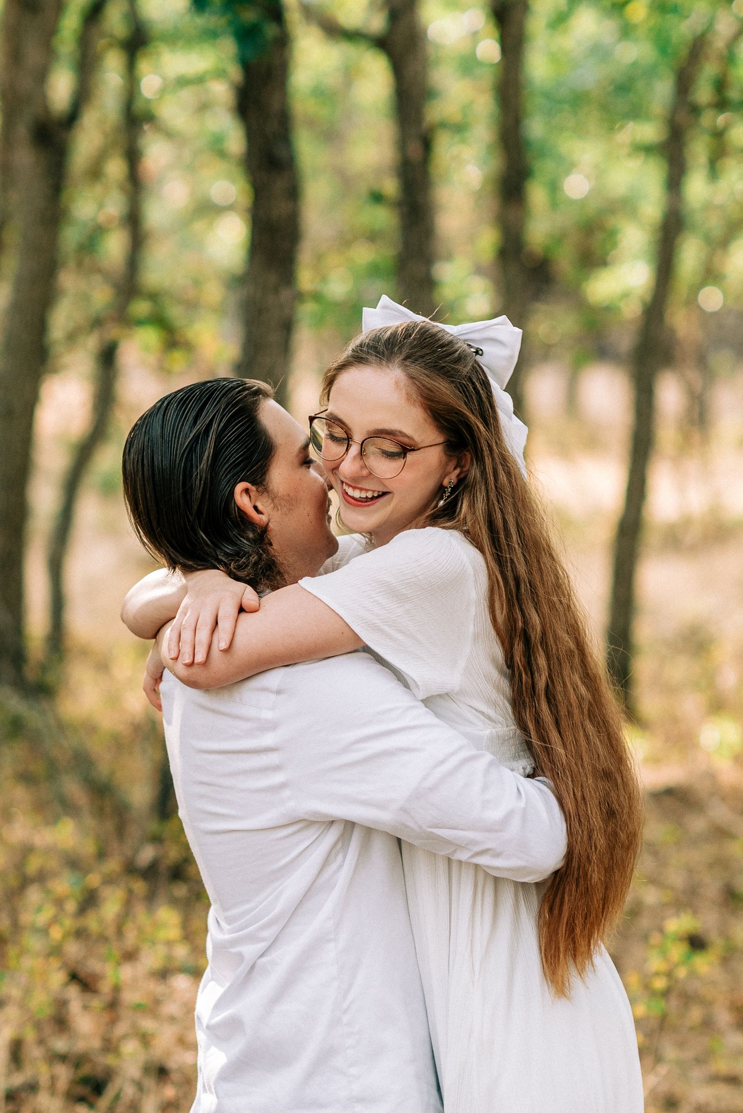 A tender embrace between a couple in white clothing among forest trees.