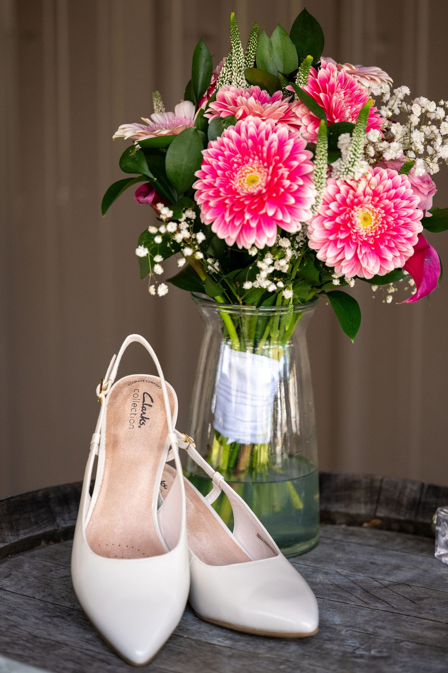 White Clarks slingback heels displayed in front of a glass vase with pink gerbera daisies and baby's breath bouquet.