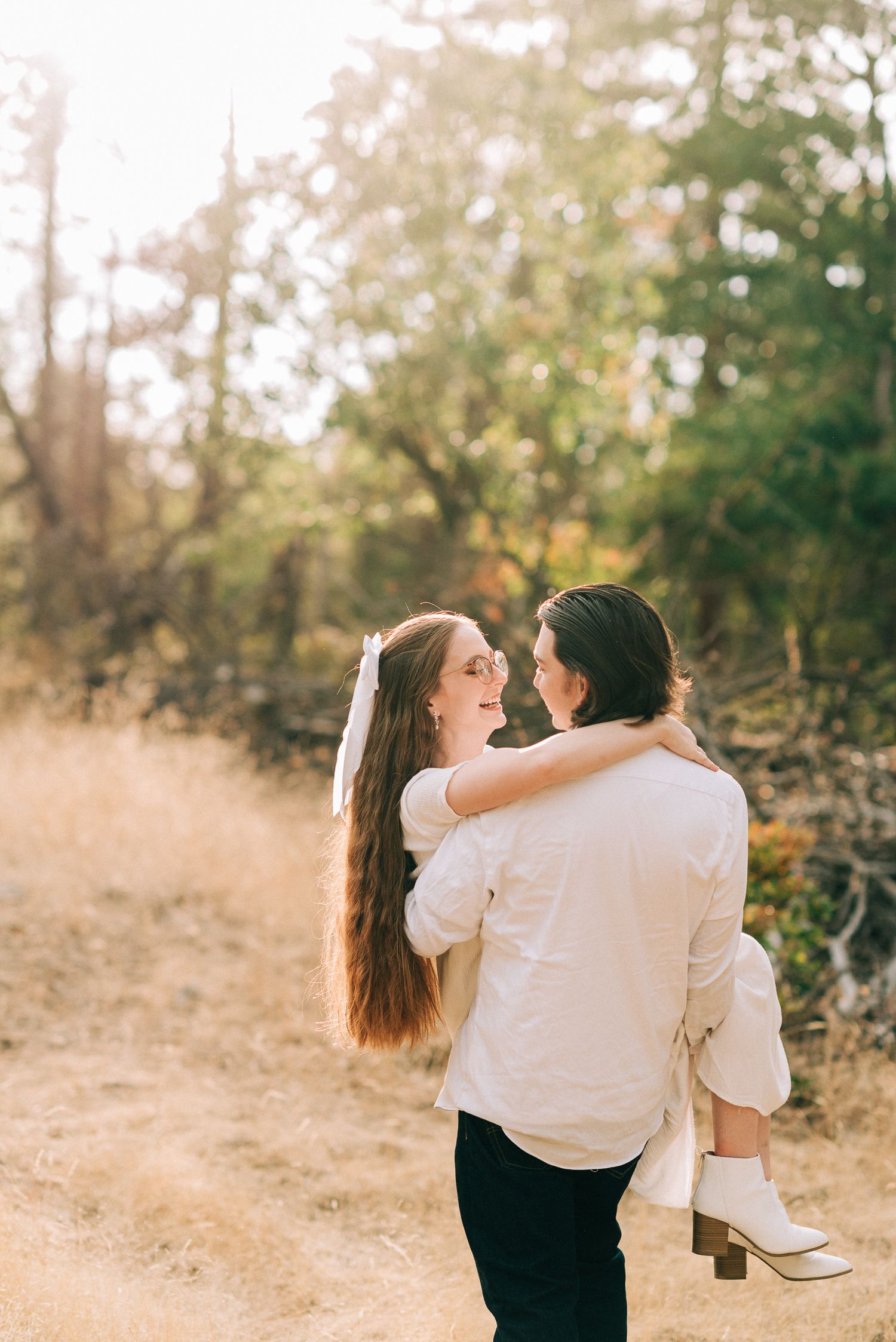 Groom carrying bride in sunlit golden field during romantic outdoor wedding portrait session in nature.