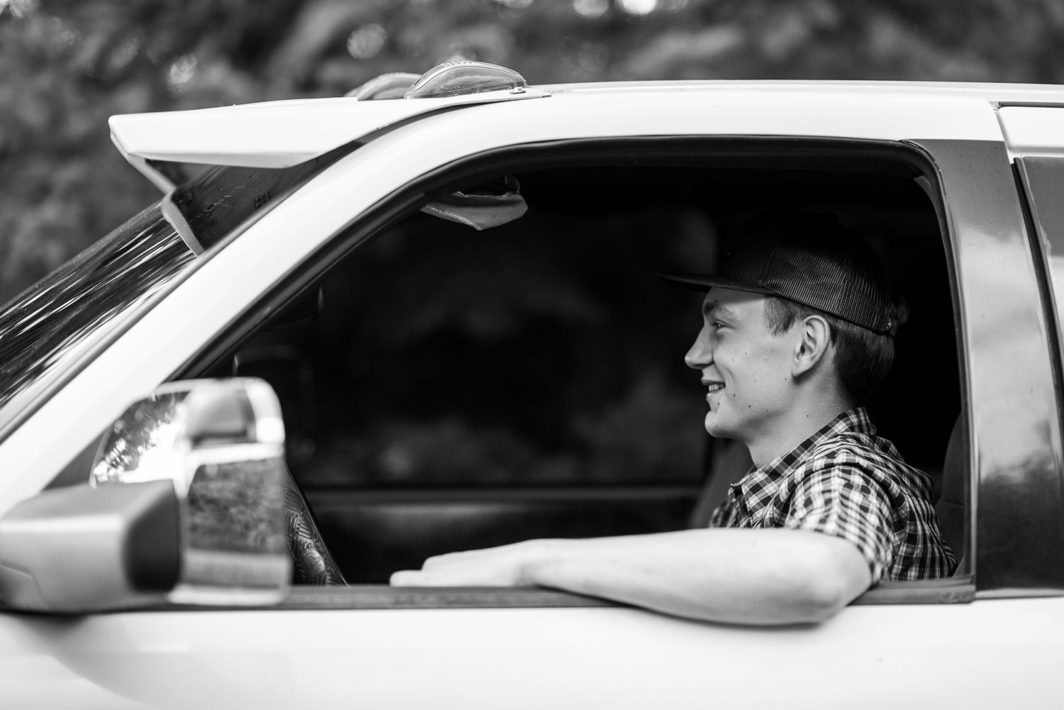 Smiling young man in cap driving a truck, captured in black and white through the window.