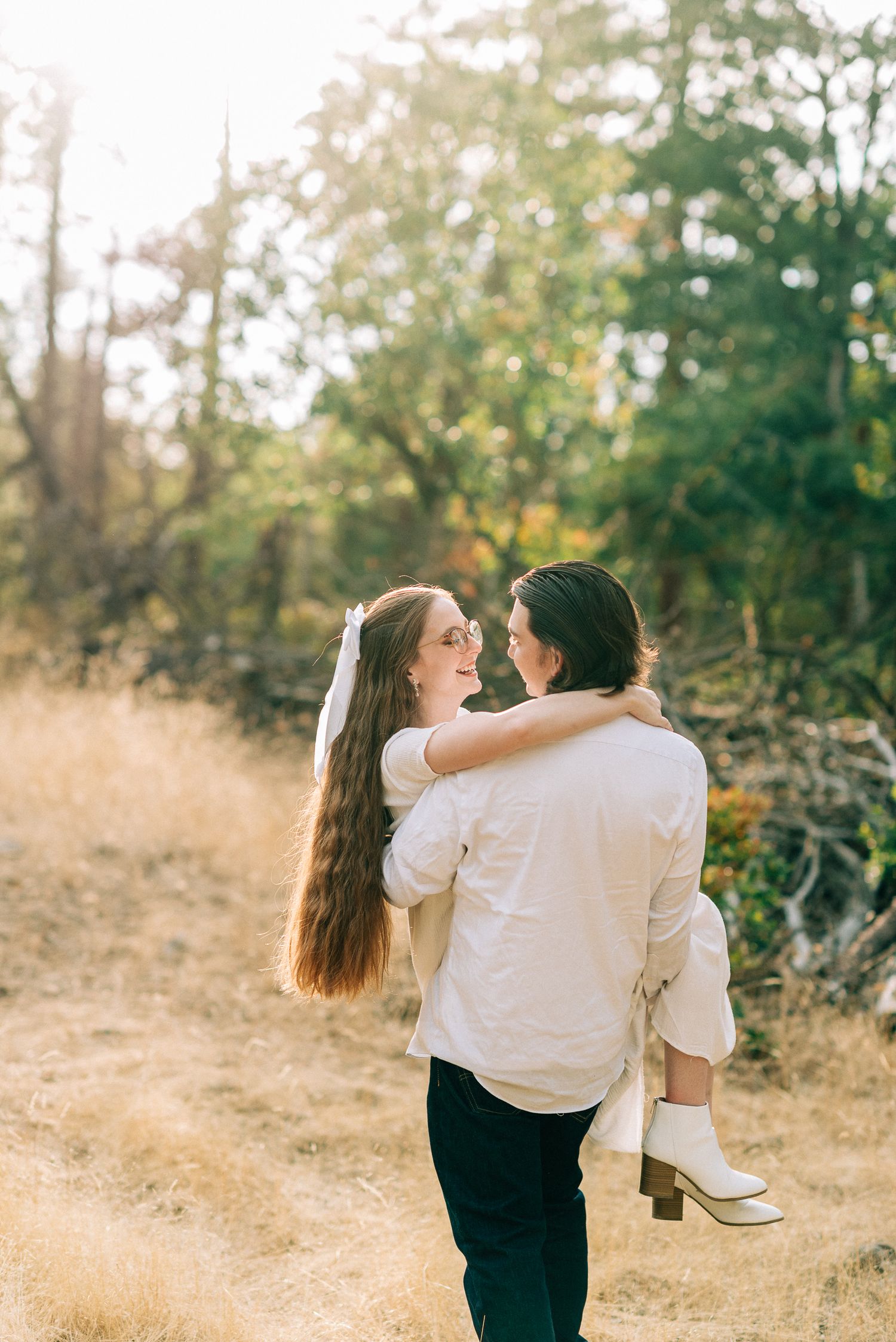 A groom carries his radiant bride through a sun-drenched golden field outdoors.
