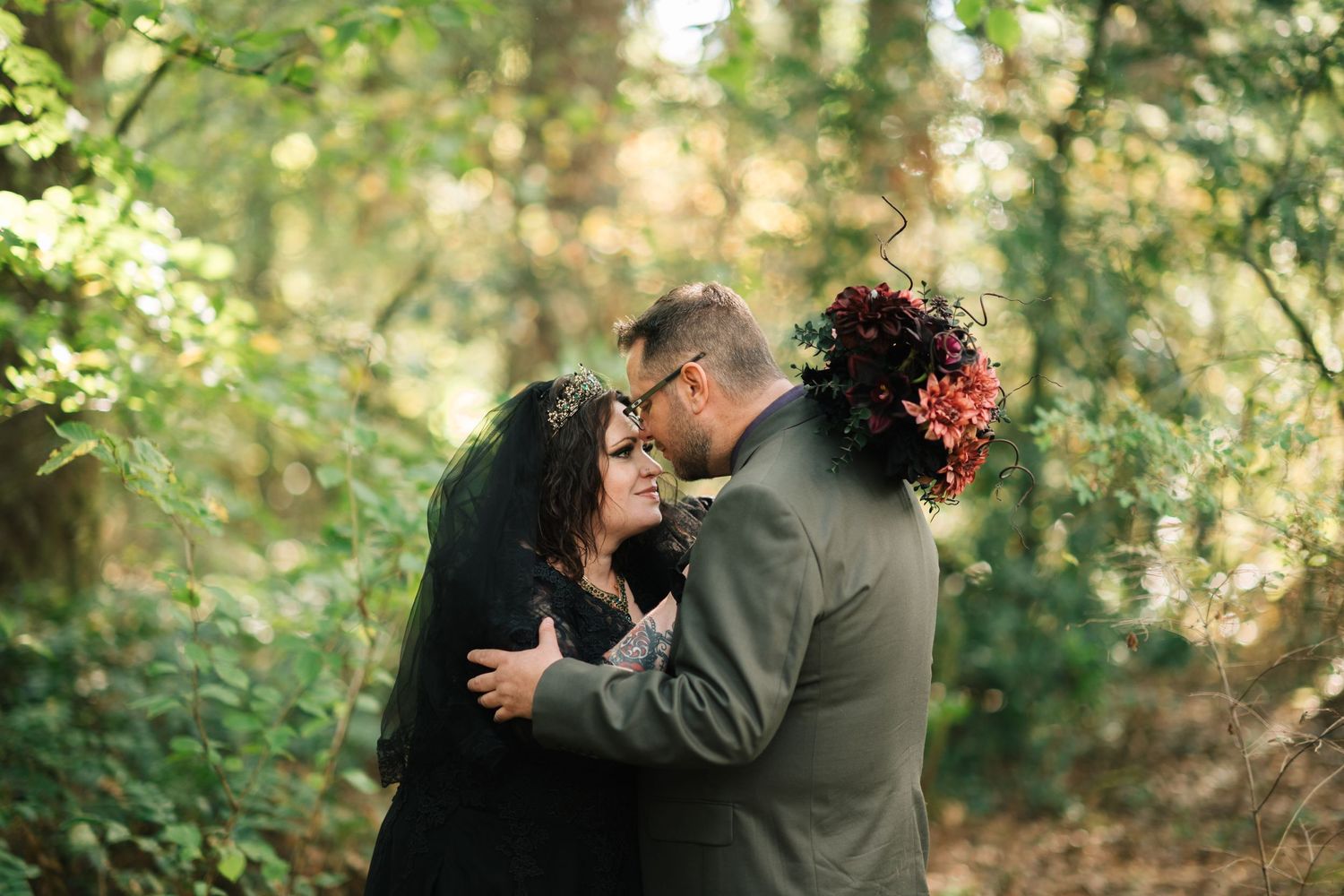 A romantic couple embraces in a sunlit forest setting during an outdoor photography session.