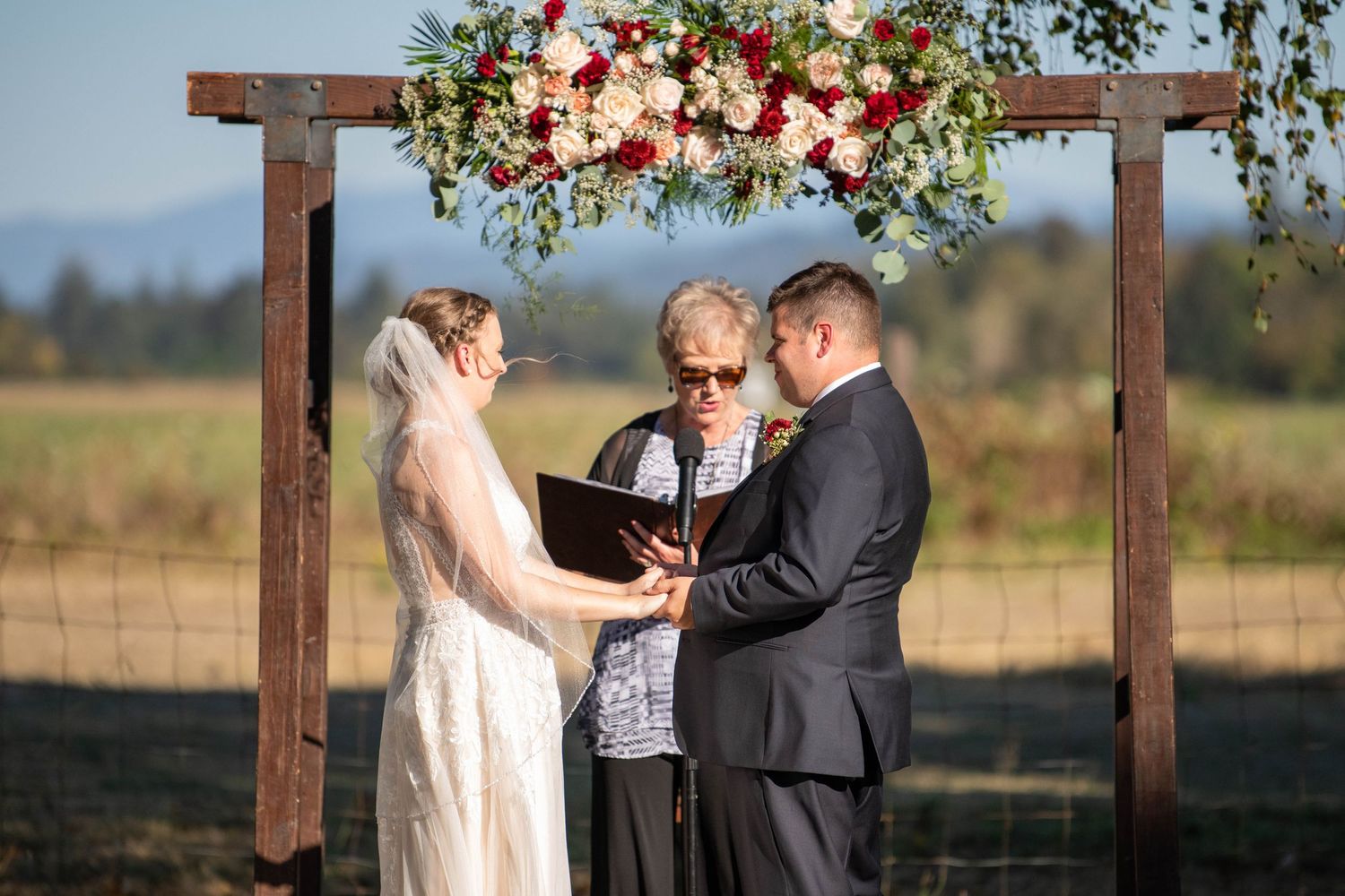 Wedding ceremony under wooden arbor decorated with pink and white floral arrangements.