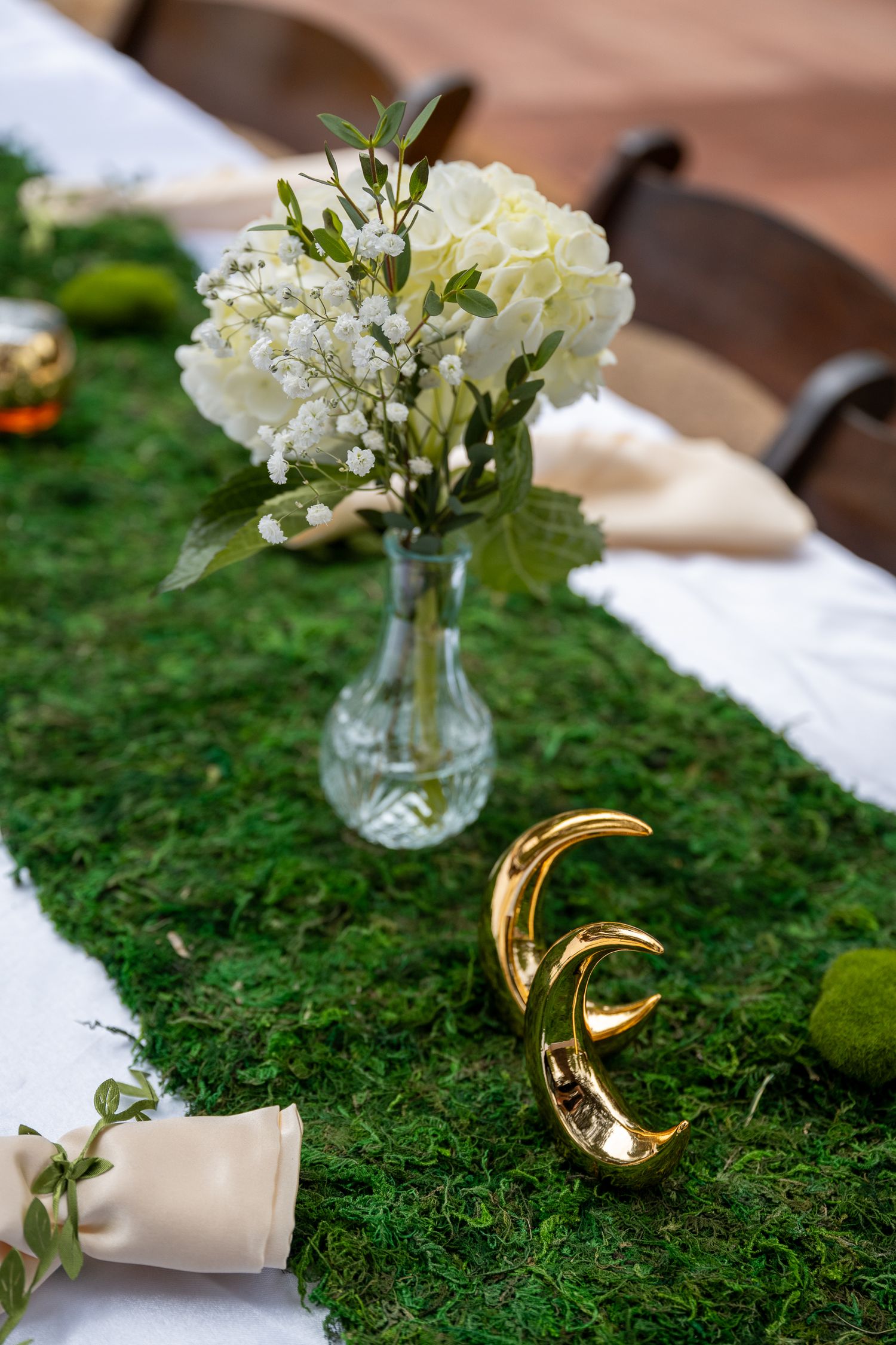 Two golden moon figures sit in front of a glass vase with white flowers on the centerpiece of a table at a wedding in the dalles, oregon