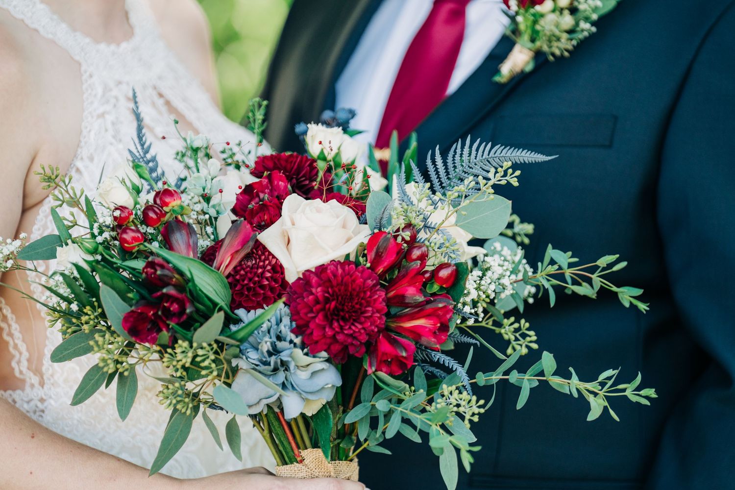 Wedding bouquets featuring deep red flowers and greenery arranged with navy blue accents.