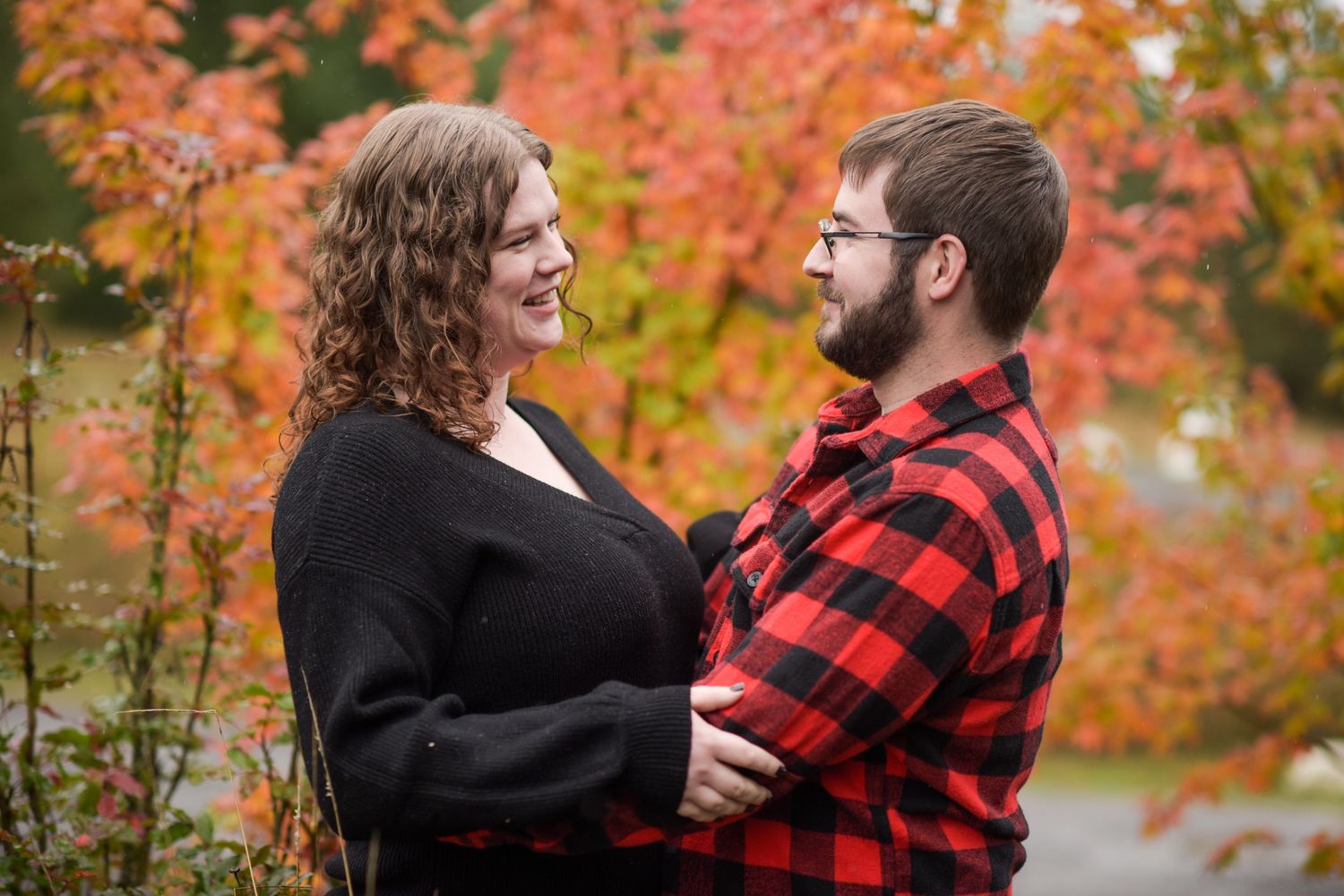 Couple sharing a laugh while embracing in front of fall colors.