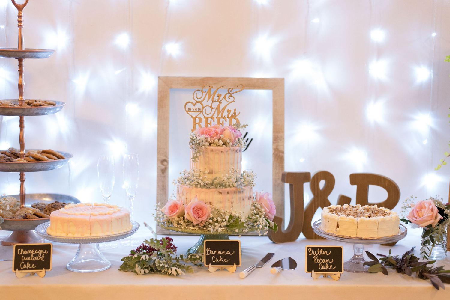 Wedding dessert table with tiered cakes and treats against a backdrop of twinkling lights.
