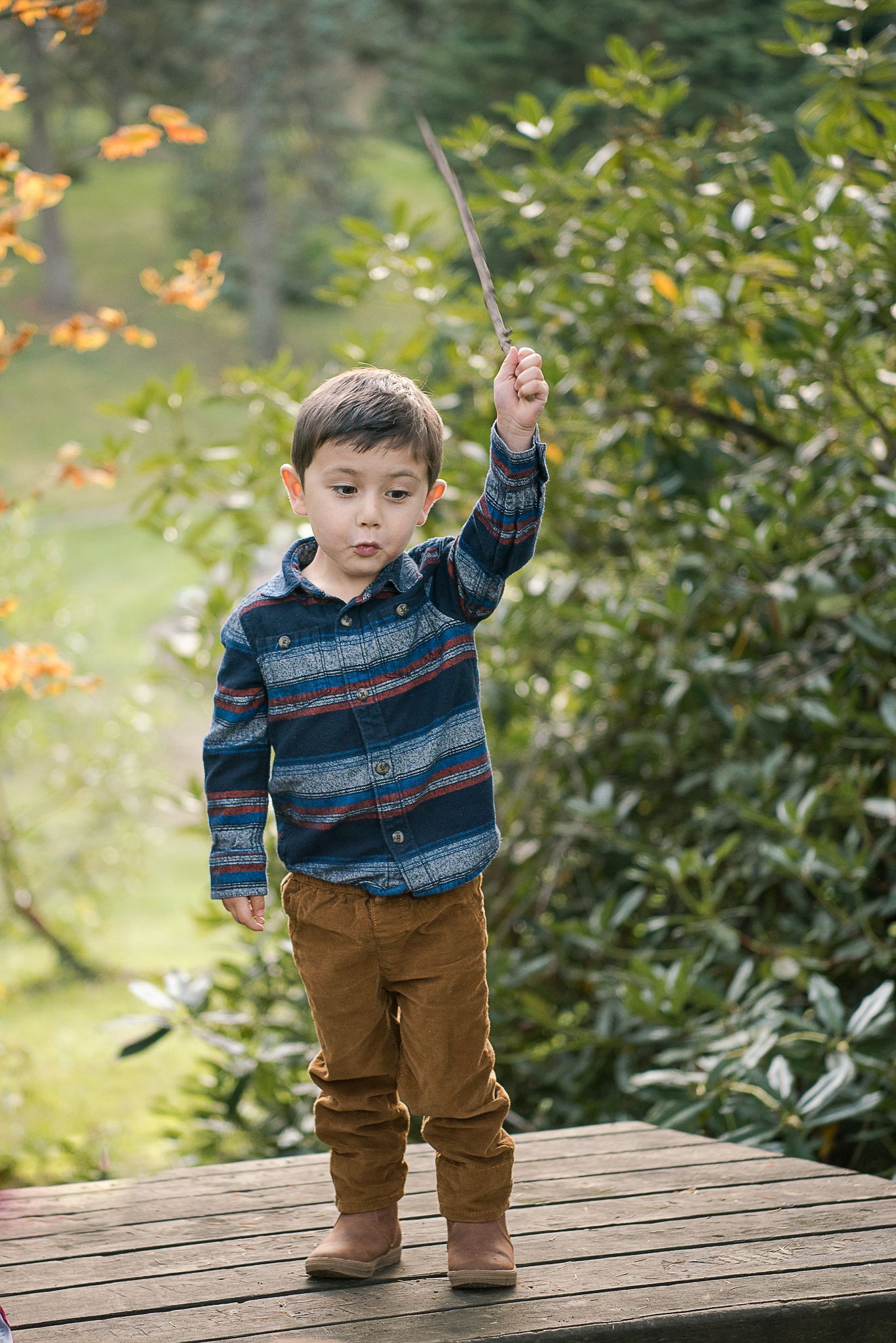 A small child in a striped sweater plays on a wooden deck outdoors.