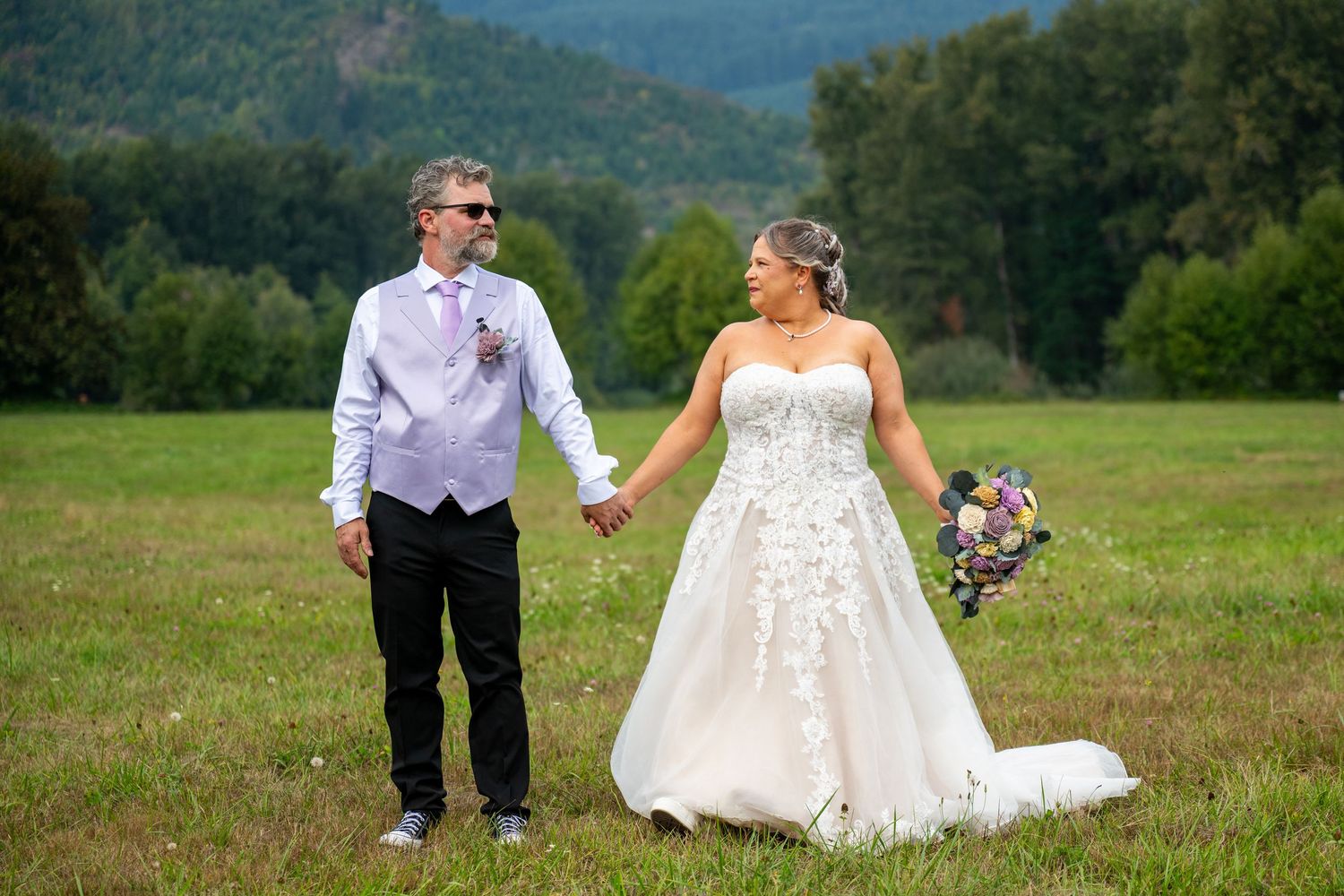 Wedding couple holding hands in a scenic mountain meadow.