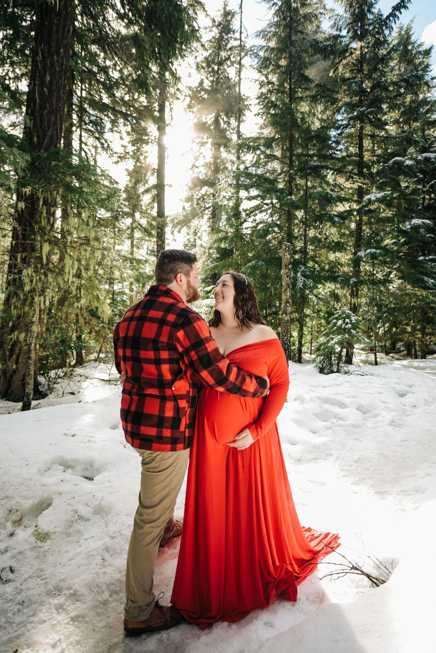 Intimate winter forest photos with couple in red dress and buffalo plaid against snowy backdrop.