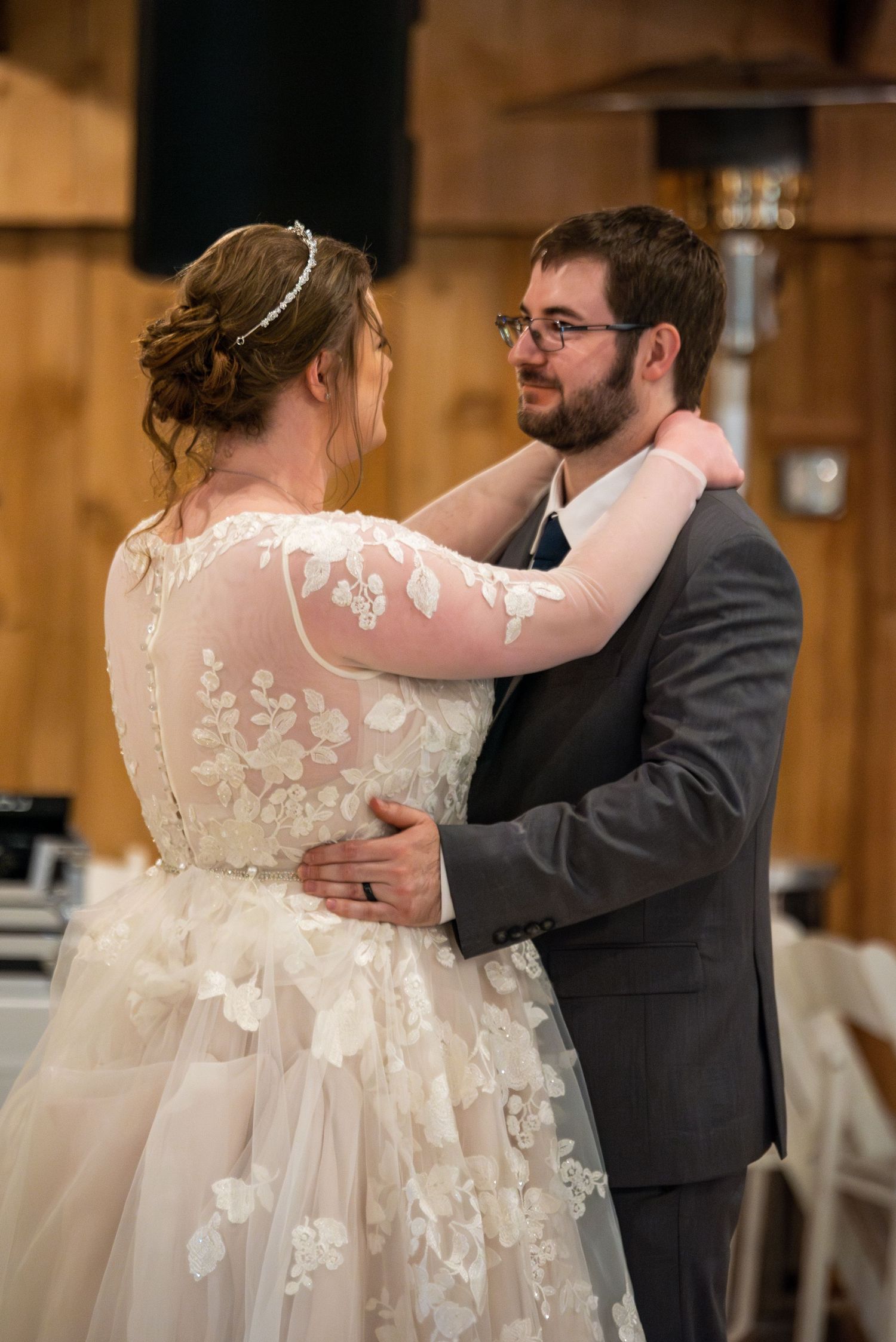 A couple shares their first dance in a rustic barn venue, with the bride wearing a detailed lace gown.