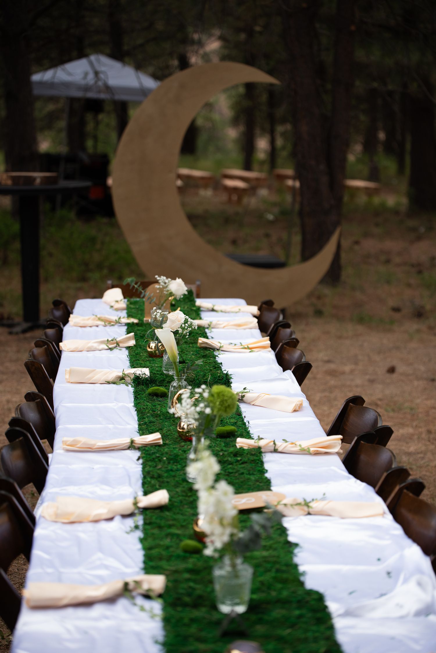 A table is set with beautiful green and white foliage and celestial accents in front of a golden crescent moon at a wedding in the dalles