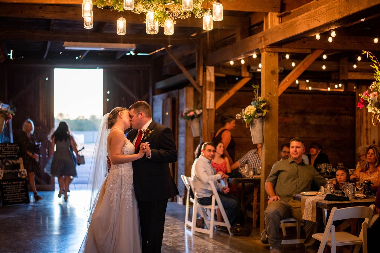 Rustic barn wedding reception with hanging Edison bulbs creating warm ambient lighting.