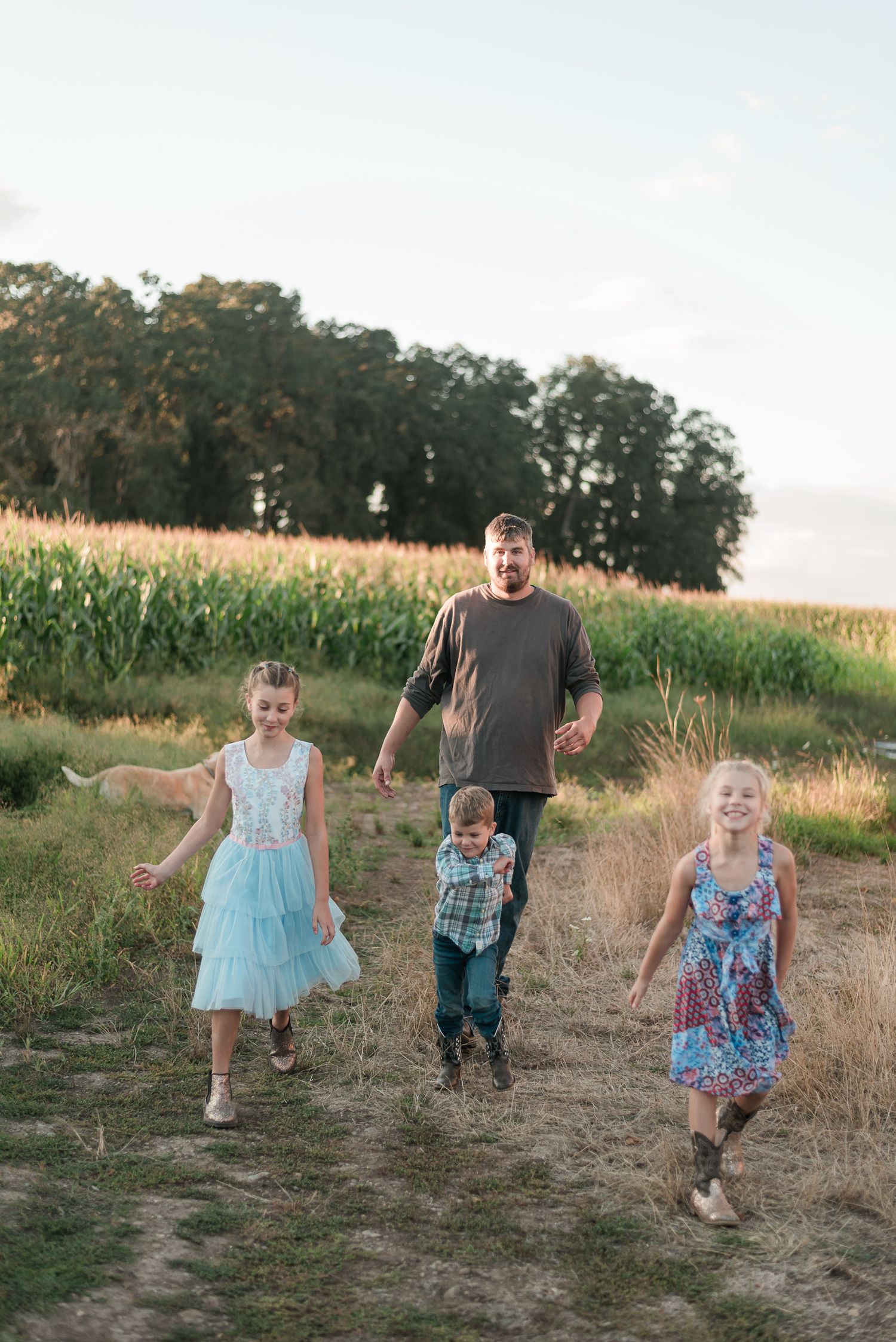 Father walking with three children through a grassy field near a cornfield during a family photo session.