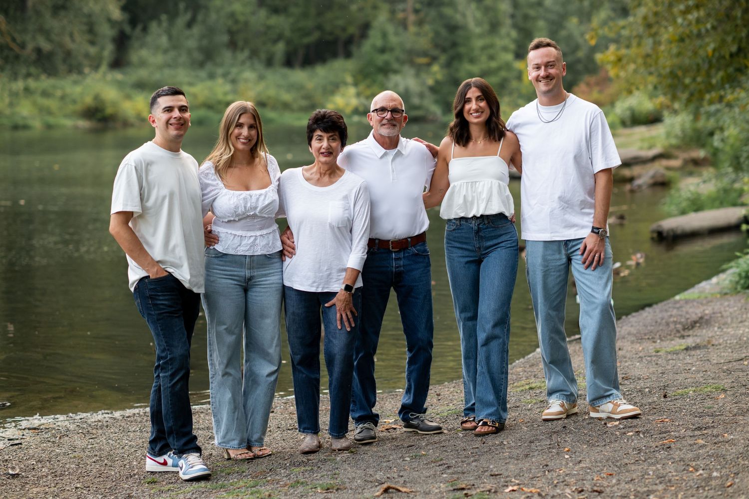 Family of six posing together in white shirts and jeans near a scenic riverside.