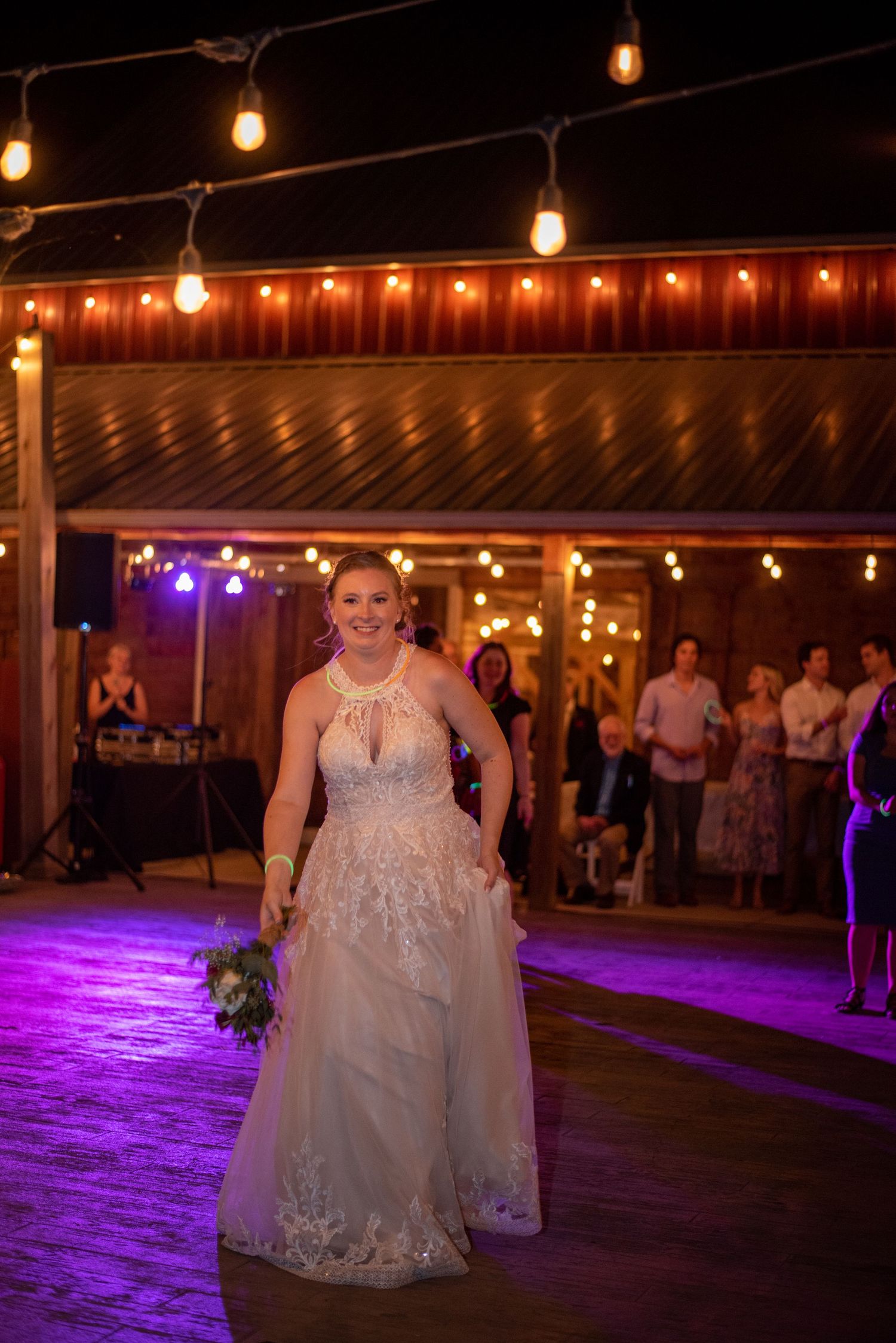 White-gowned figure dancing under glowing string lights at an outdoor evening celebration.