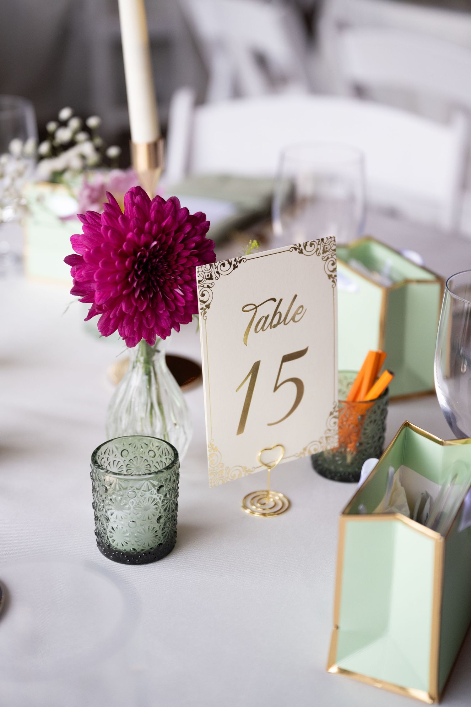 Elegant wedding table 15 centerpiece with magenta dahlia, mint green decor, gold accents, and candles on white linen.