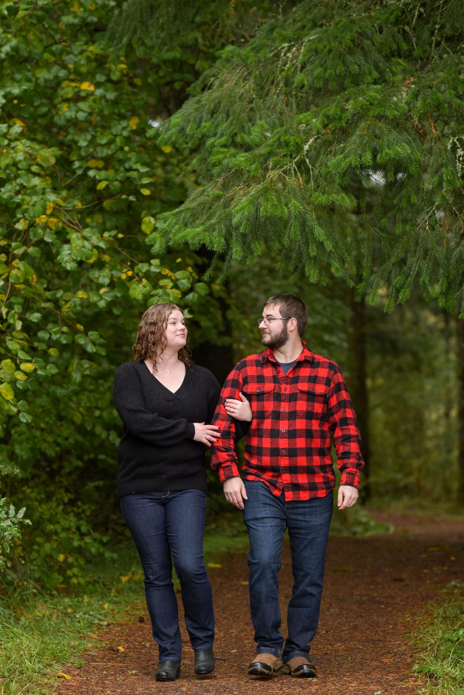 A couple walks hand in hand down a forest trail wearing matching casual outfits.