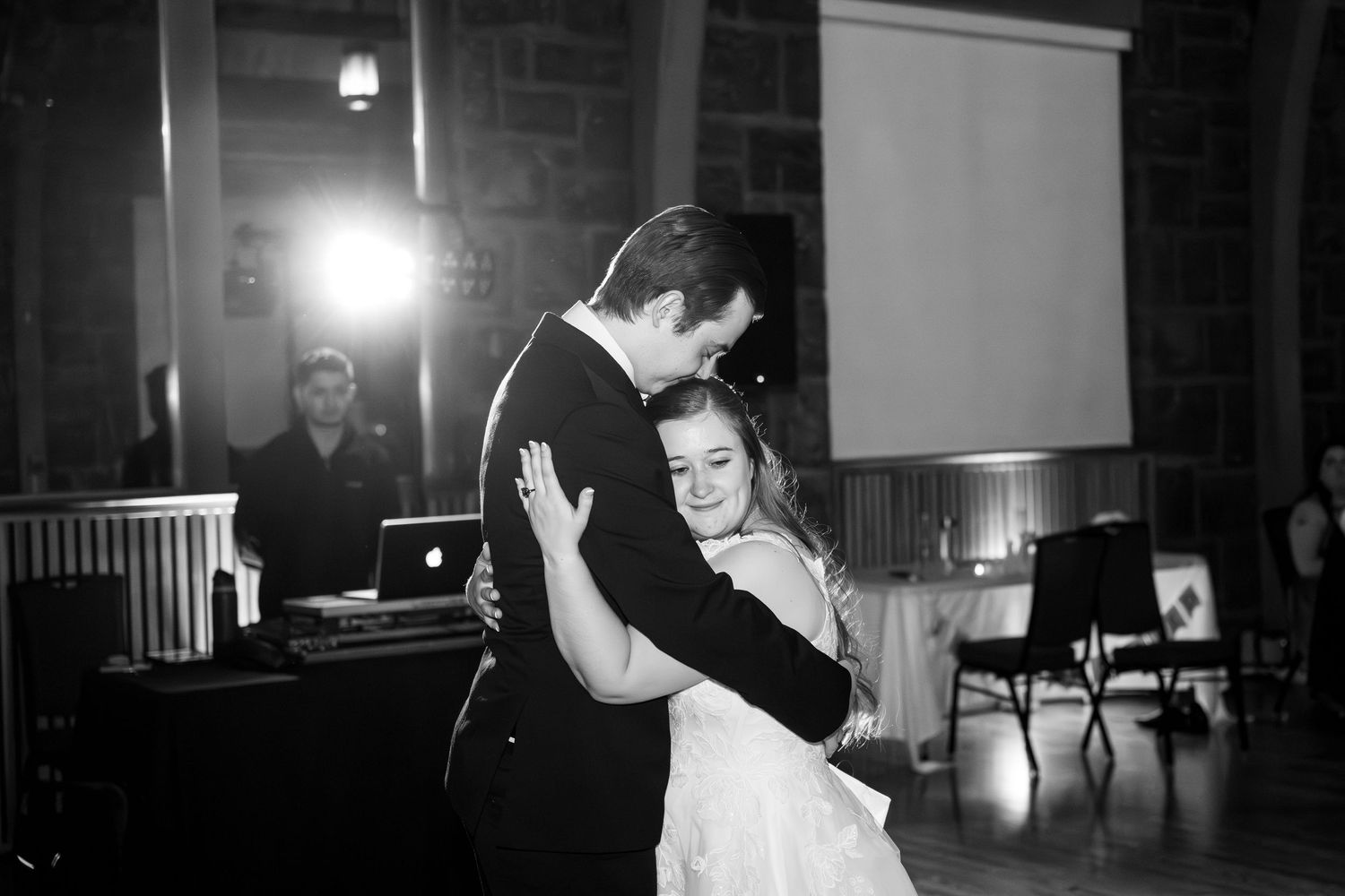 Bride and groom share their first dance in black and white at a wedding reception with a DJ in the background.