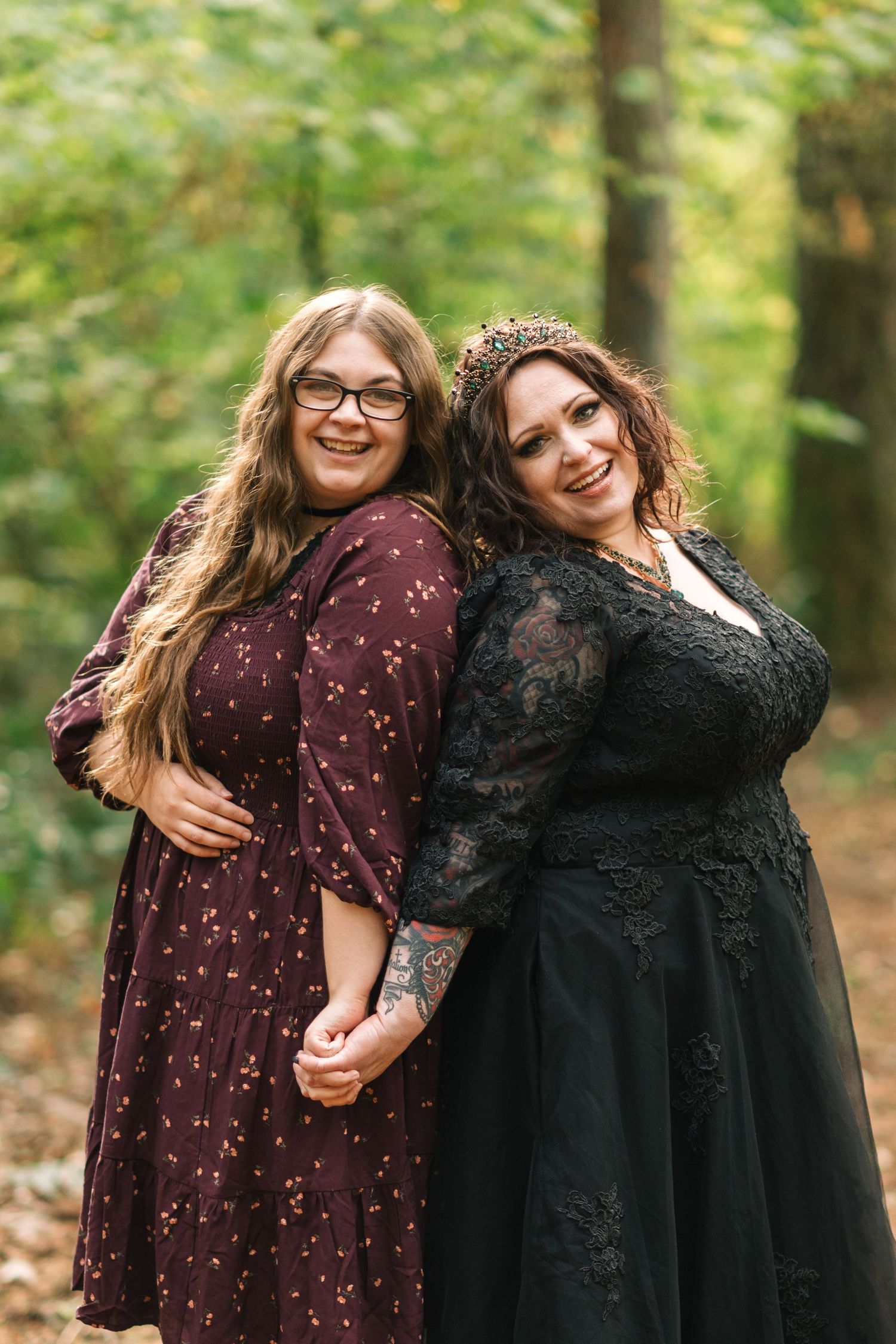 Two friends in autumn dresses share joyful moments together in a forest setting with fallen leaves.
