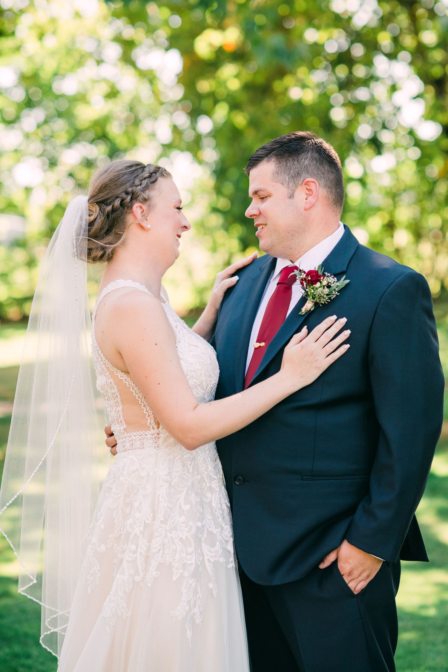 Couple shares intimate moments in a garden setting with sunlit trees in the background.