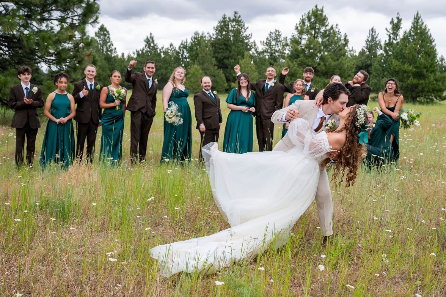 Groom dips bride for a kiss as bridal party cheers in the background
