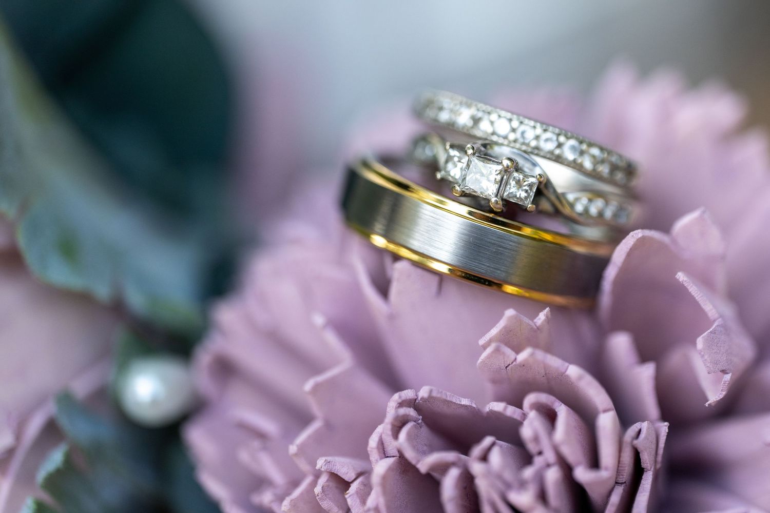 Wedding rings rest on delicate pink flower petals in a macro shot.