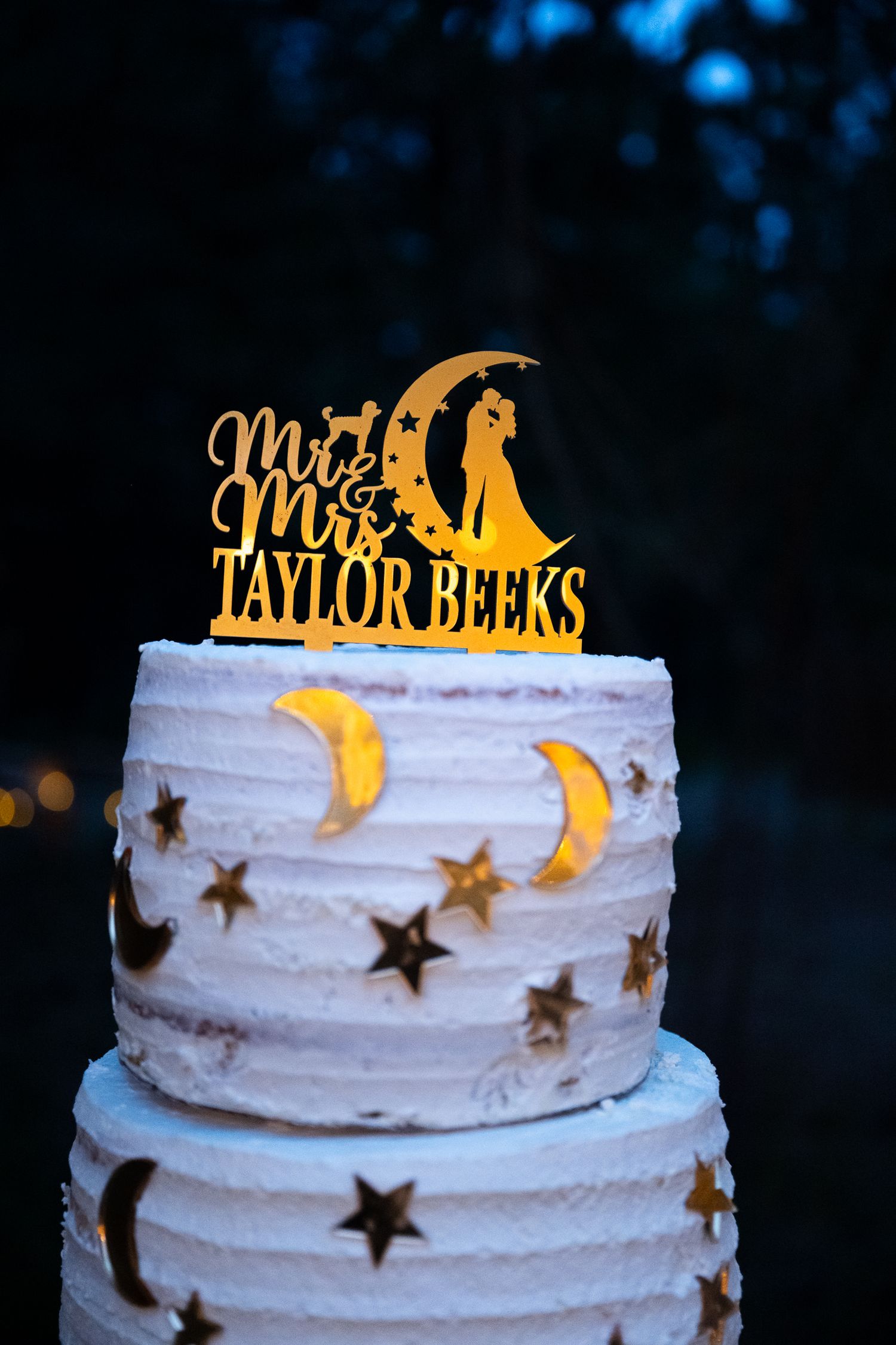 Two-tier white wedding cake decorated with gold stars and moons topped with Mr. & Mrs. Taylor Beeks topper.