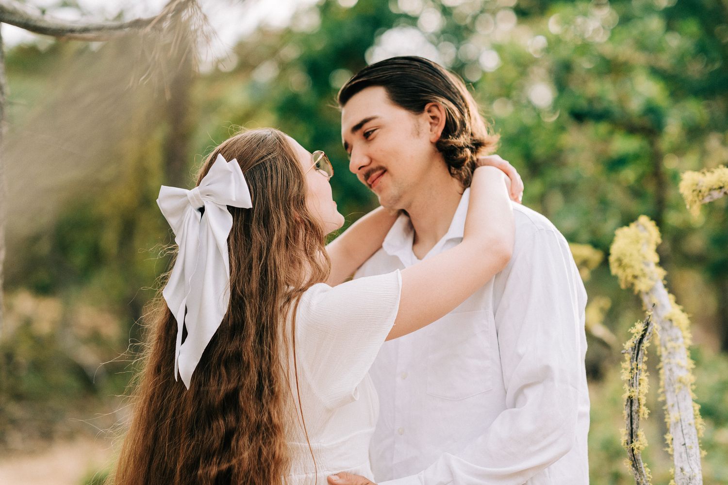 Couple in white outfits share intimate moments in a sunlit outdoor setting.