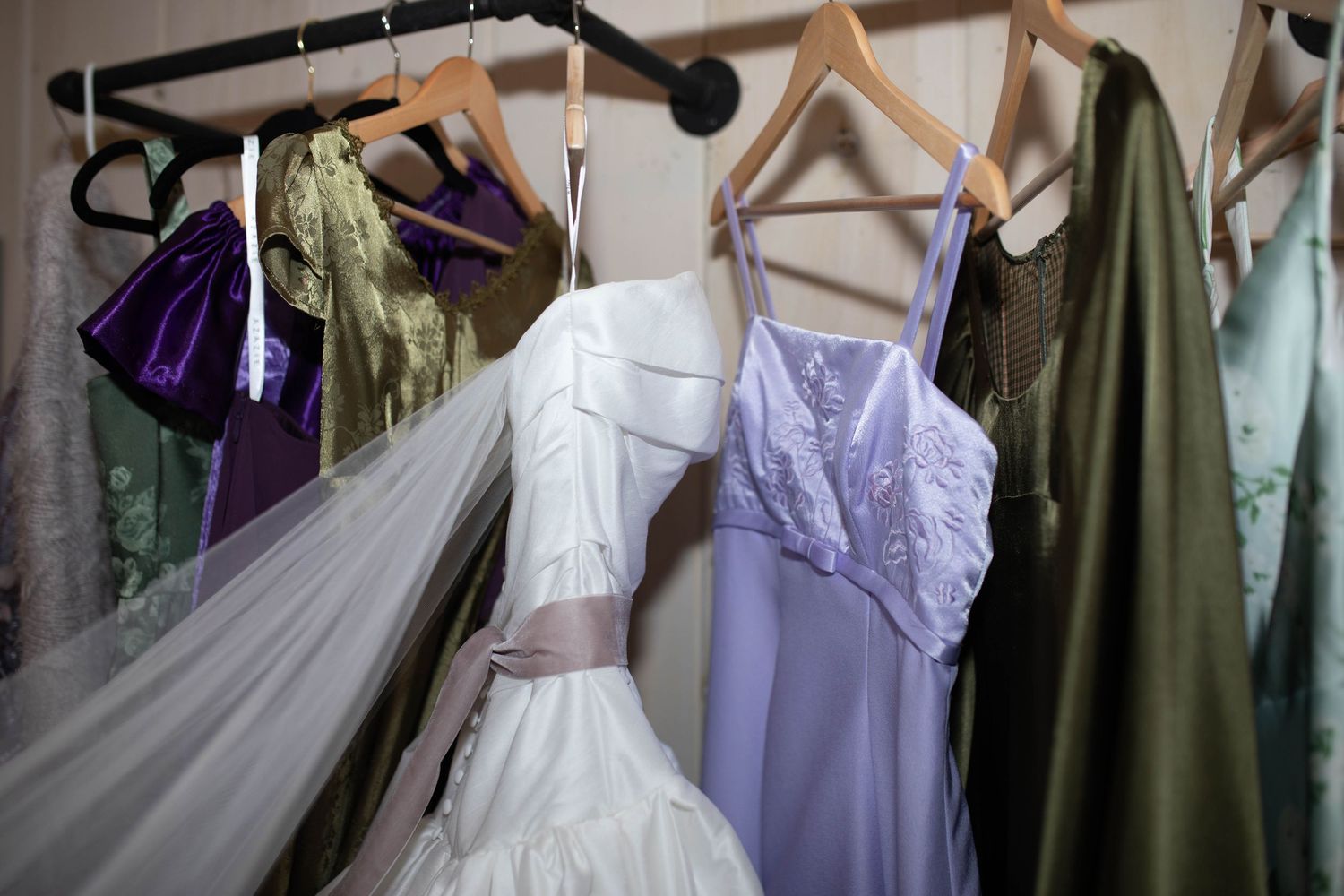 Wedding dresses and colorful gowns hanging on a rack including white bridal gown with veil and ribbon.