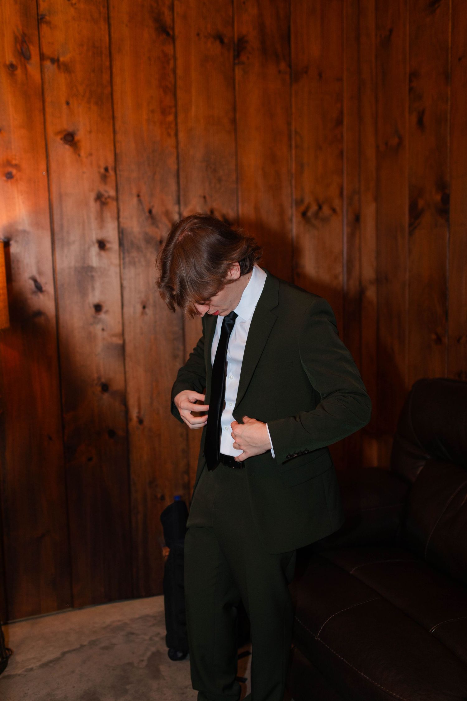 Groom in dark suit adjusting jacket against wood panel wall in warm indoor lighting before micro wedding in Nashville.