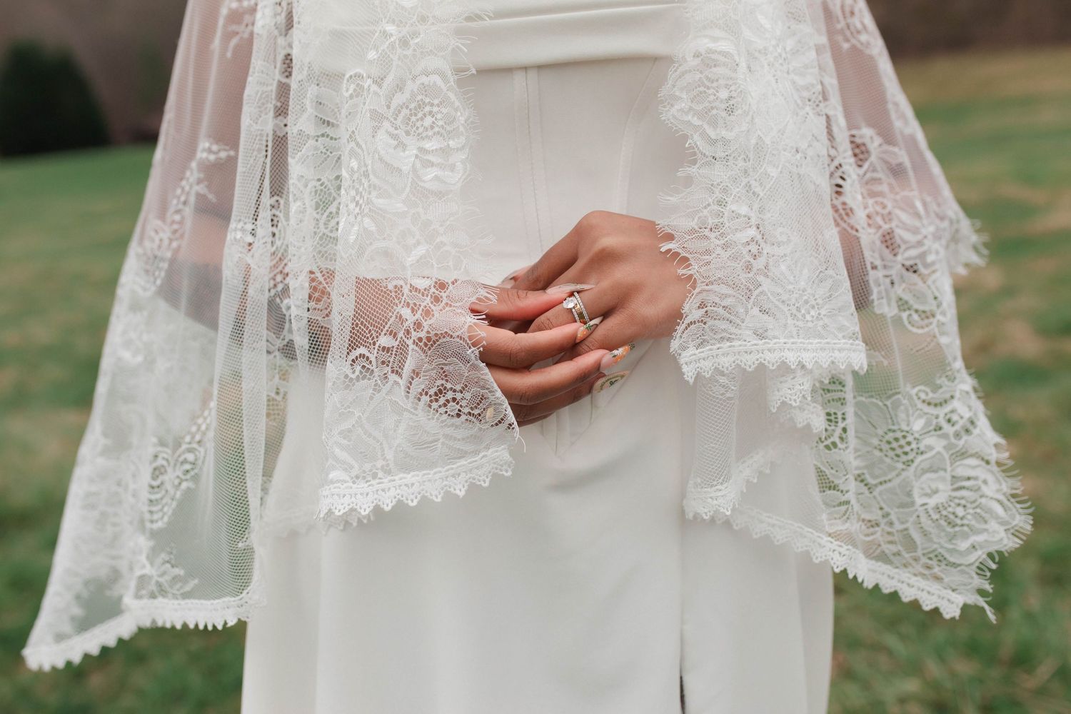 Close-up of bride's hands clasped over white gown with intricate lace veil and diamond wedding ring after eloping in Nashville.
