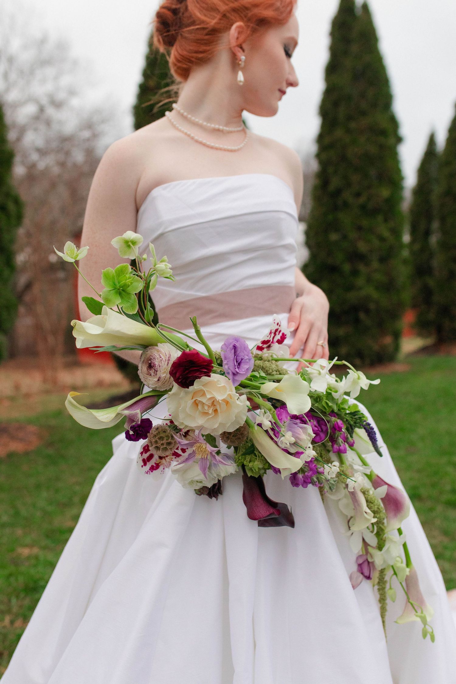 Red-haired bride in strapless gown holding lush cascading floral bouquet outdoors after eloping in Nashville.