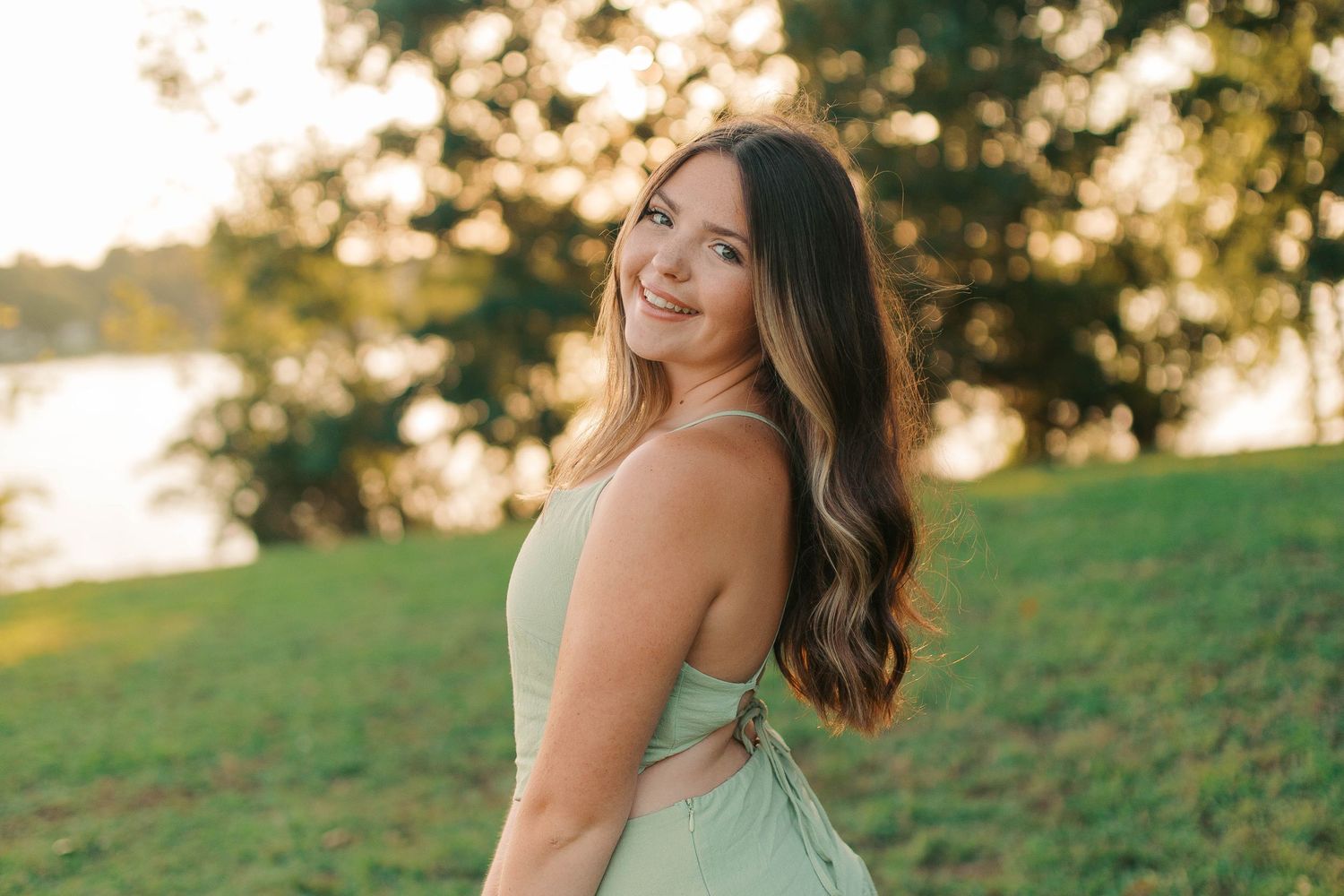 Young woman in mint green dress smiling over shoulder in sunny park.
